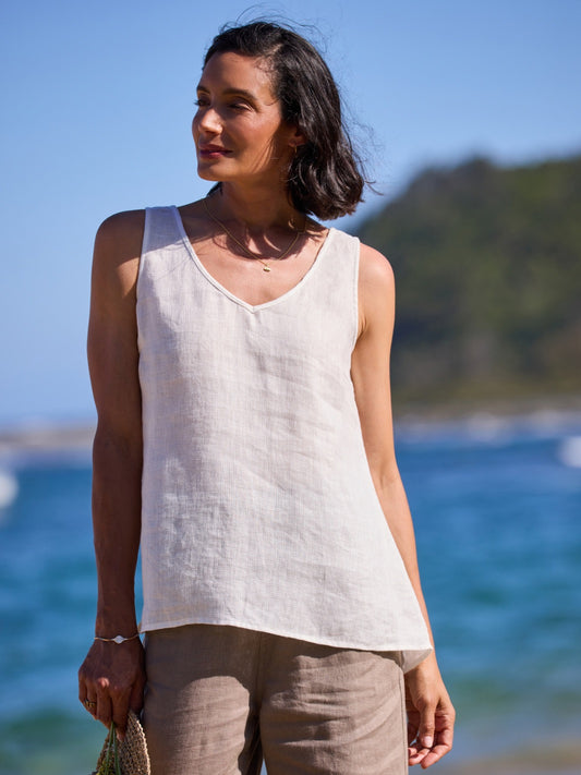 Woman wearing a white sleeveless top and beige pants standing by the ocean.