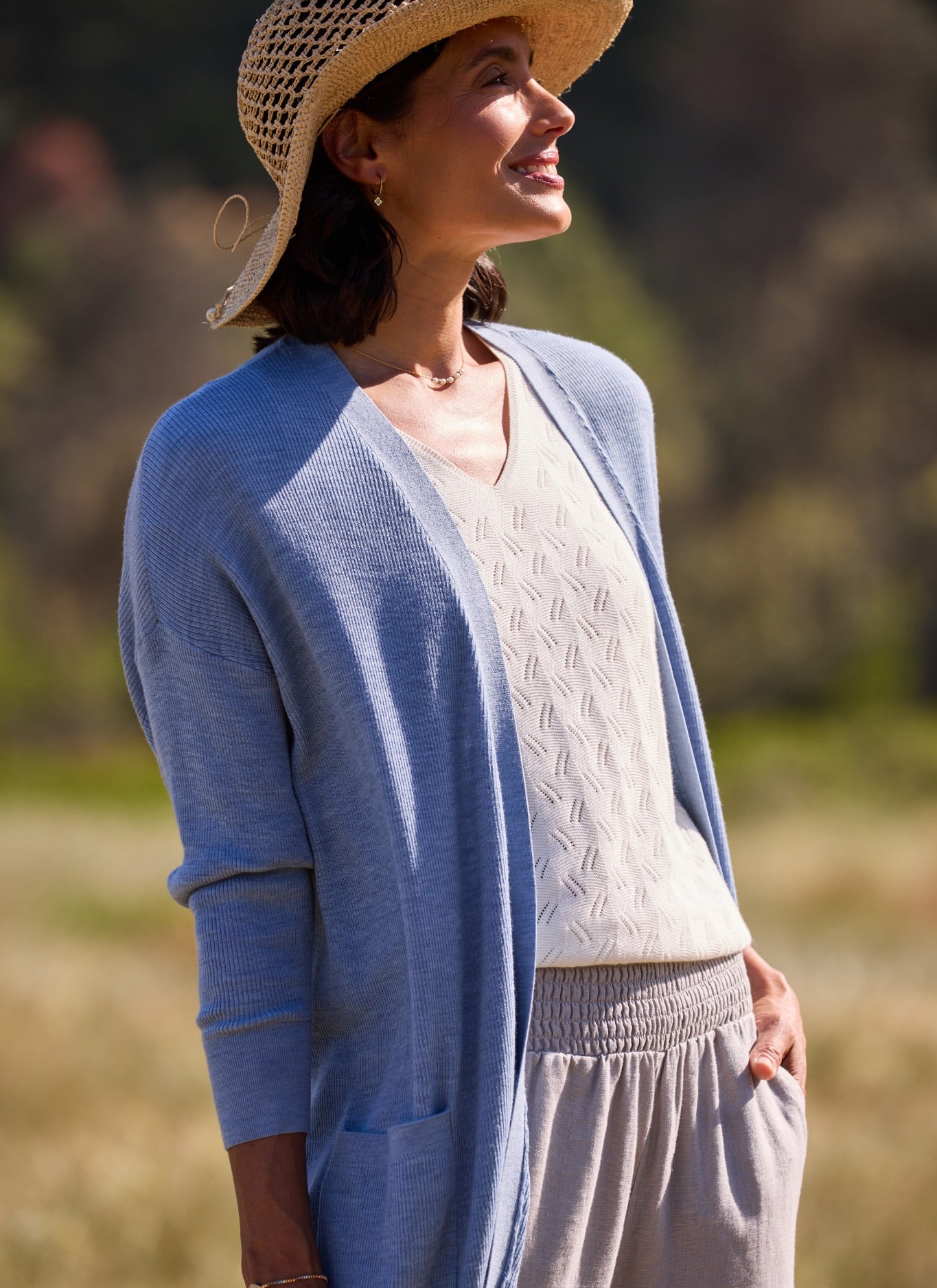 Woman wearing a blue cardigan, white top, and straw hat in an outdoor setting