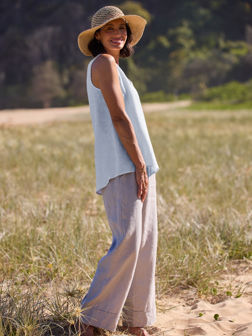 Woman wearing a light blue sleeveless top and beige pants standing in a field.