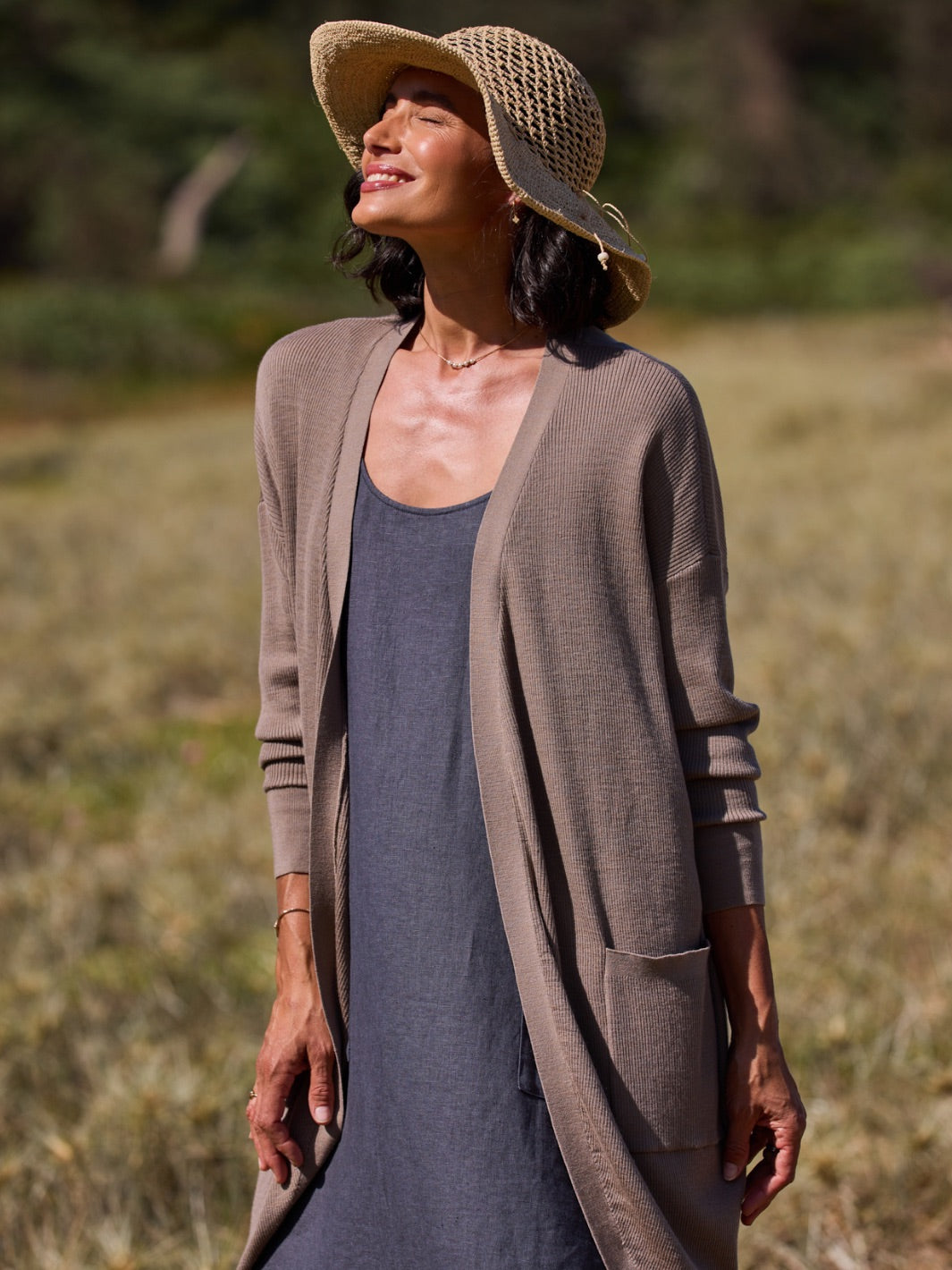 Woman wearing a brown cardigan and straw hat in a natural setting
