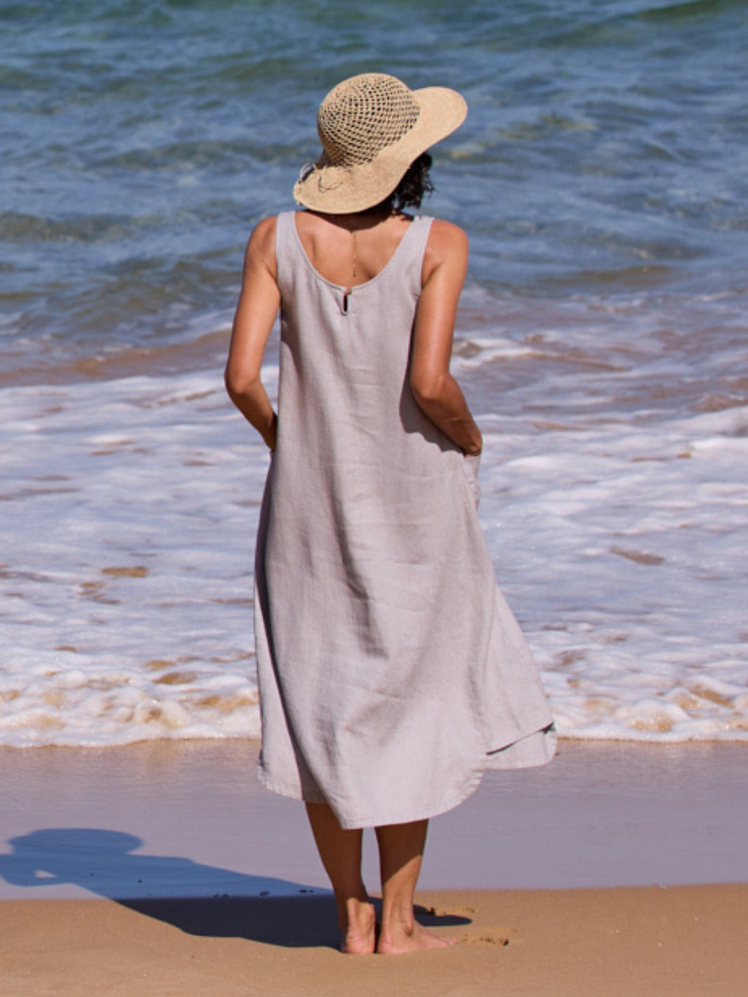 Woman in a light dress and sun hat standing on a beach