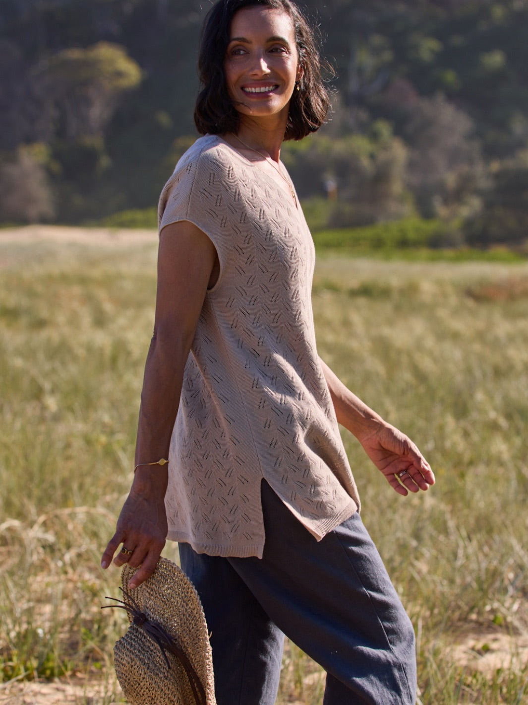 Woman walking in a field wearing a beige top and dark pants.
