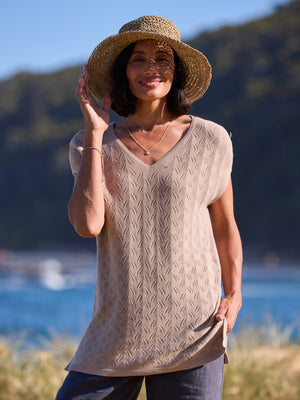 Woman wearing a beige top and straw hat by a body of water.