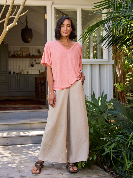 Woman in a pink top and beige pants standing on a wooden deck with plants in the background