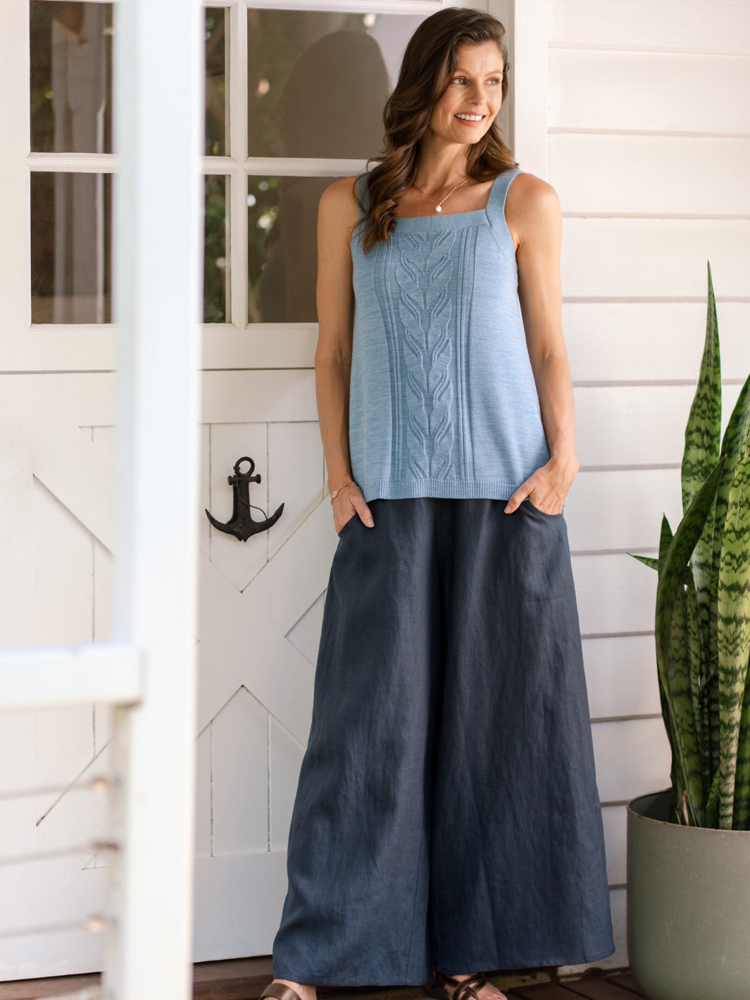 Woman wearing a blue sleeveless top and dark blue wide-leg pants standing on a porch.