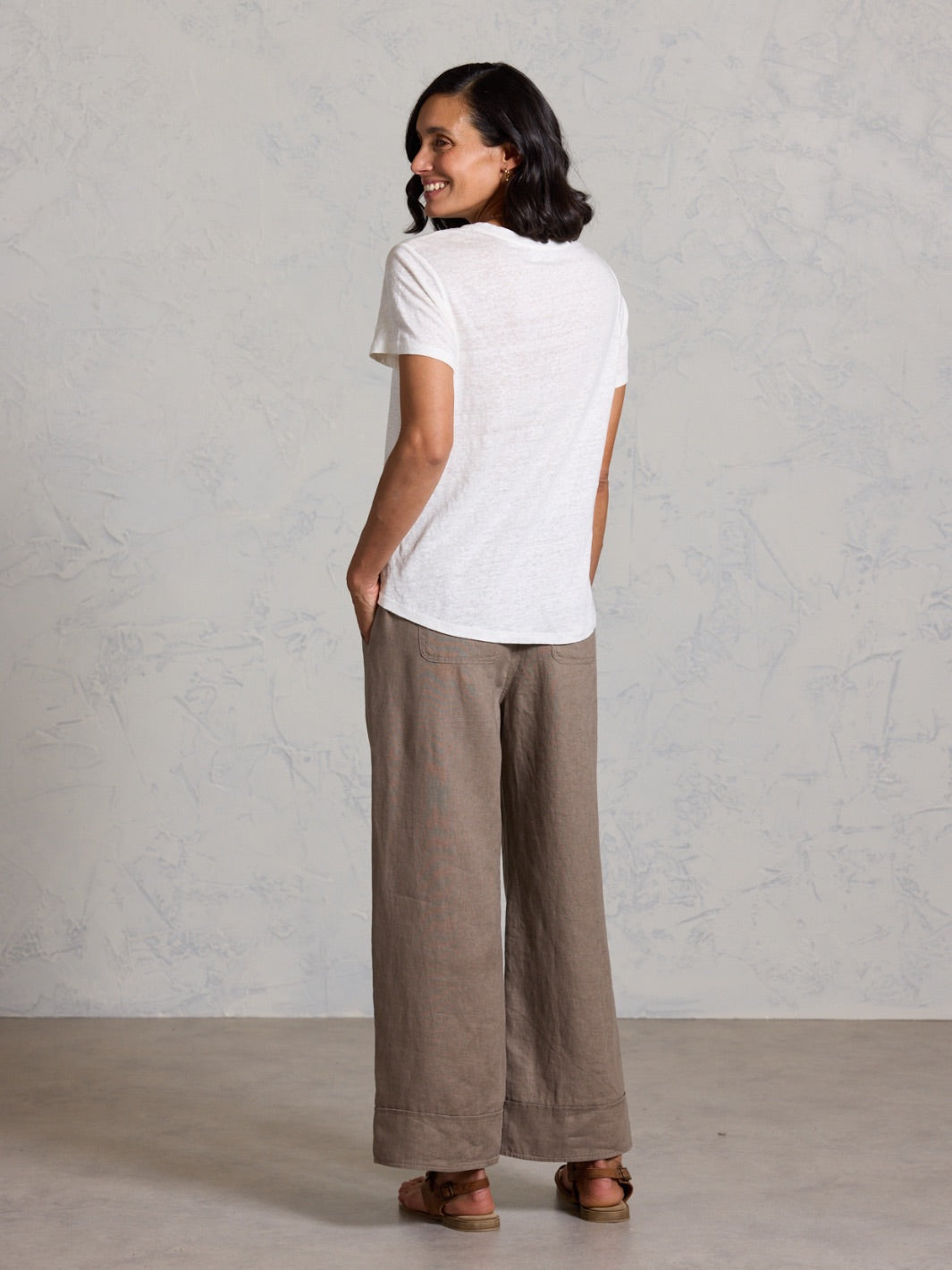 Woman wearing a white t-shirt and brown wide-leg pants against a plain background