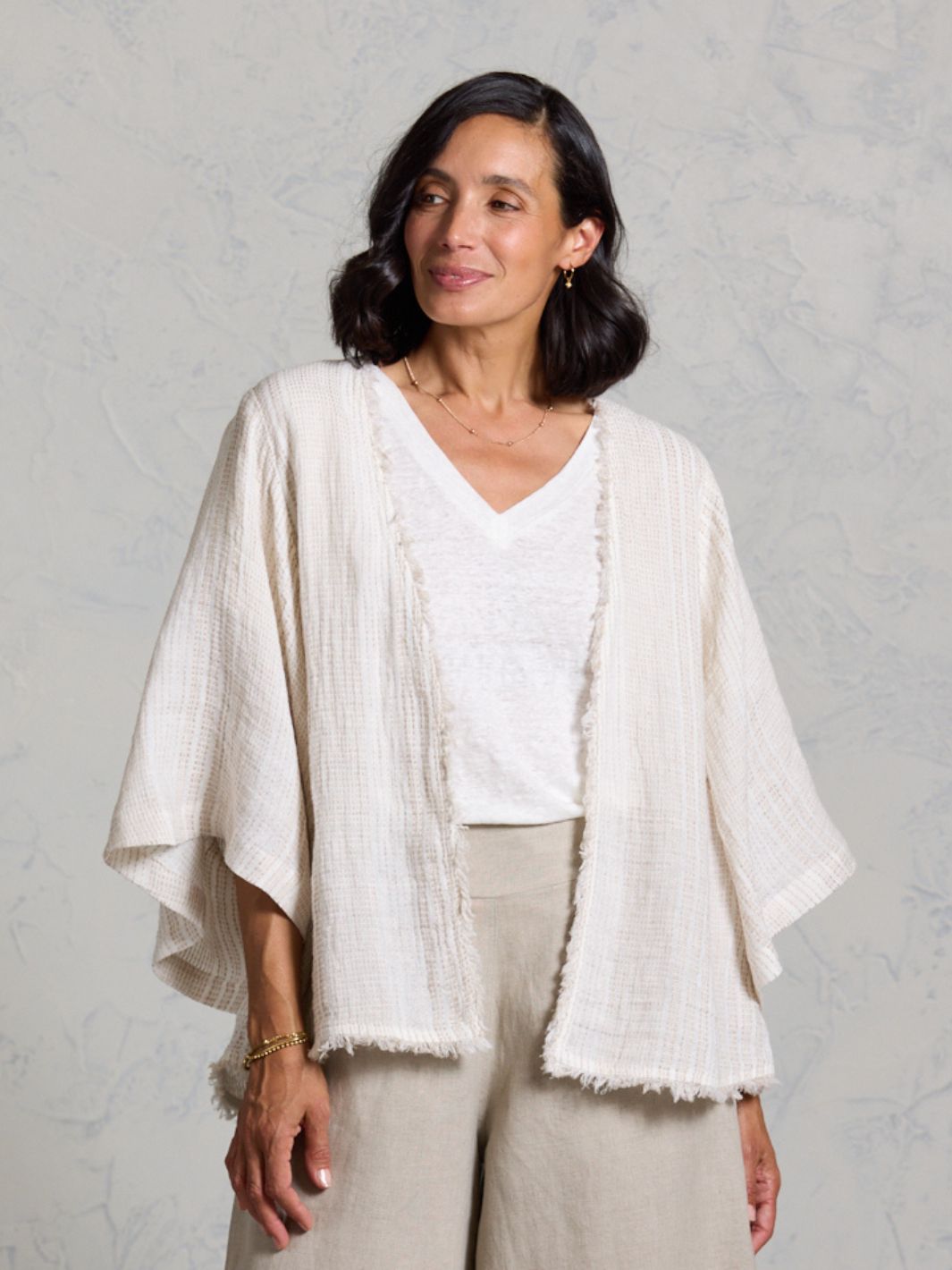 Woman wearing a white top and beige kimono-style garment against a gray background