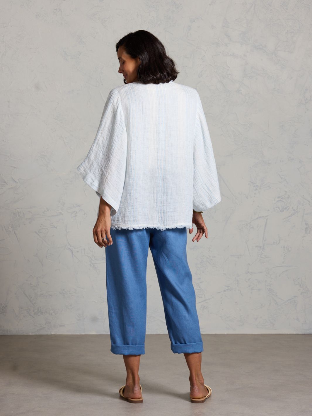 Woman wearing a white top and blue pants against a plain background