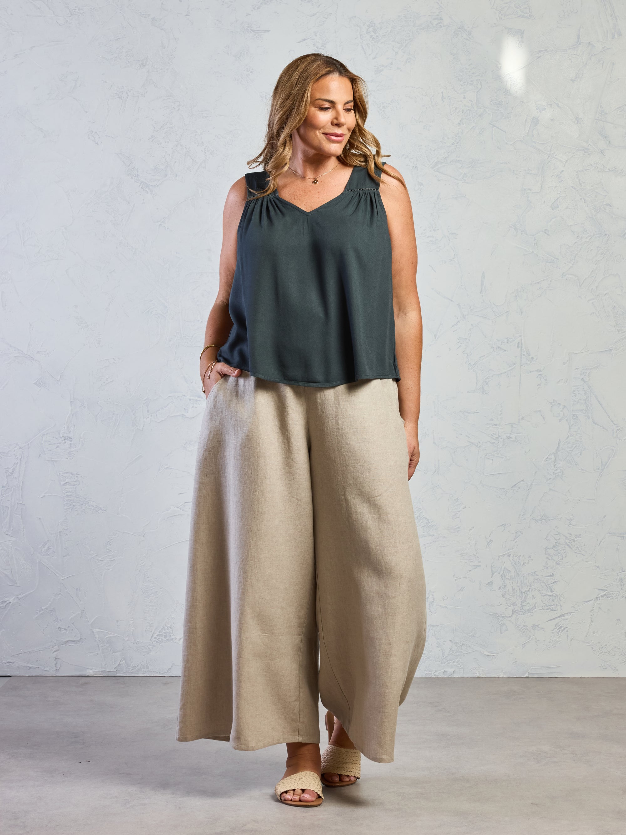 Woman wearing a black sleeveless top and beige wide-leg pants against a light gray background