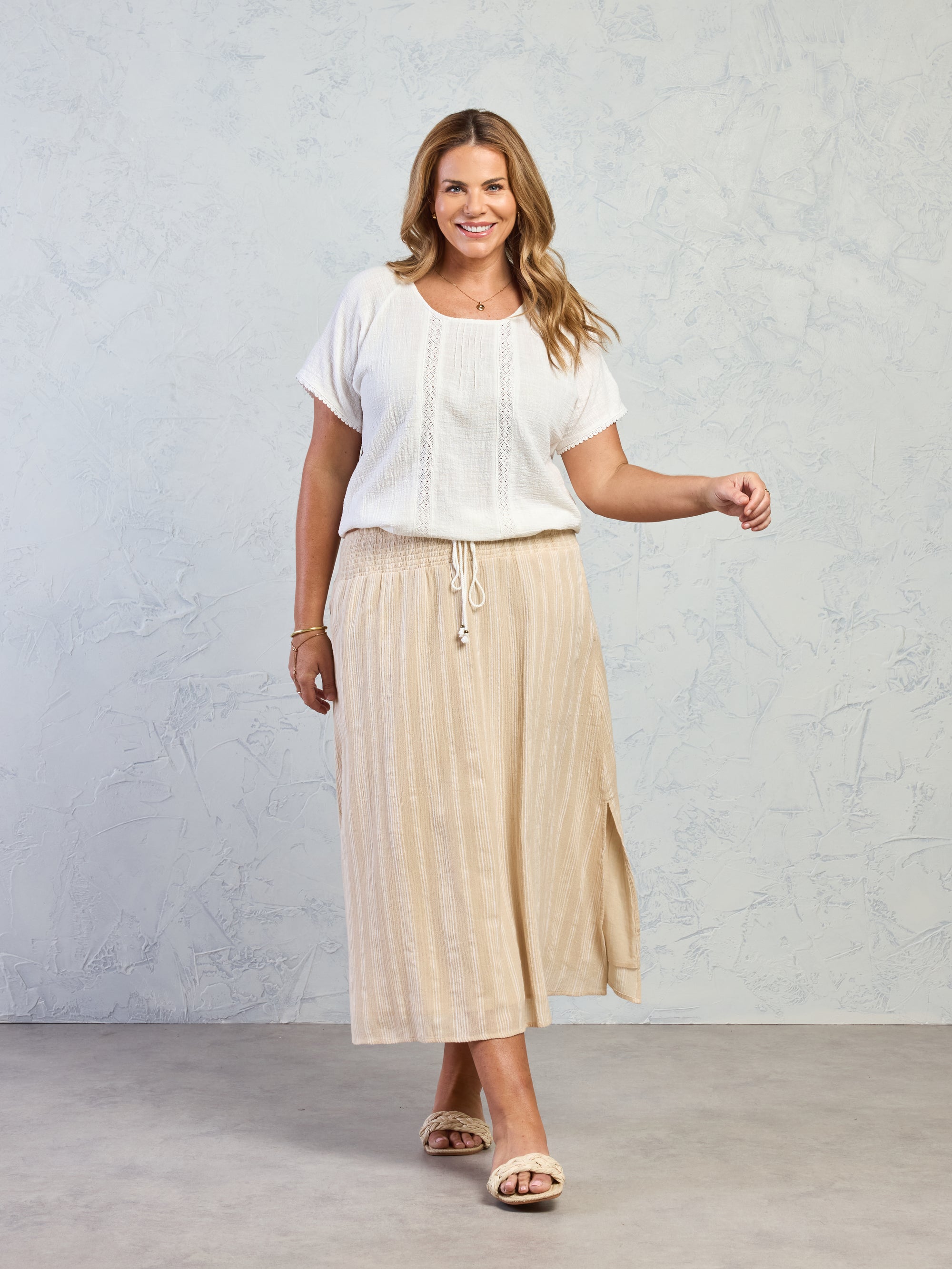 Woman wearing a white top and beige skirt against a plain background