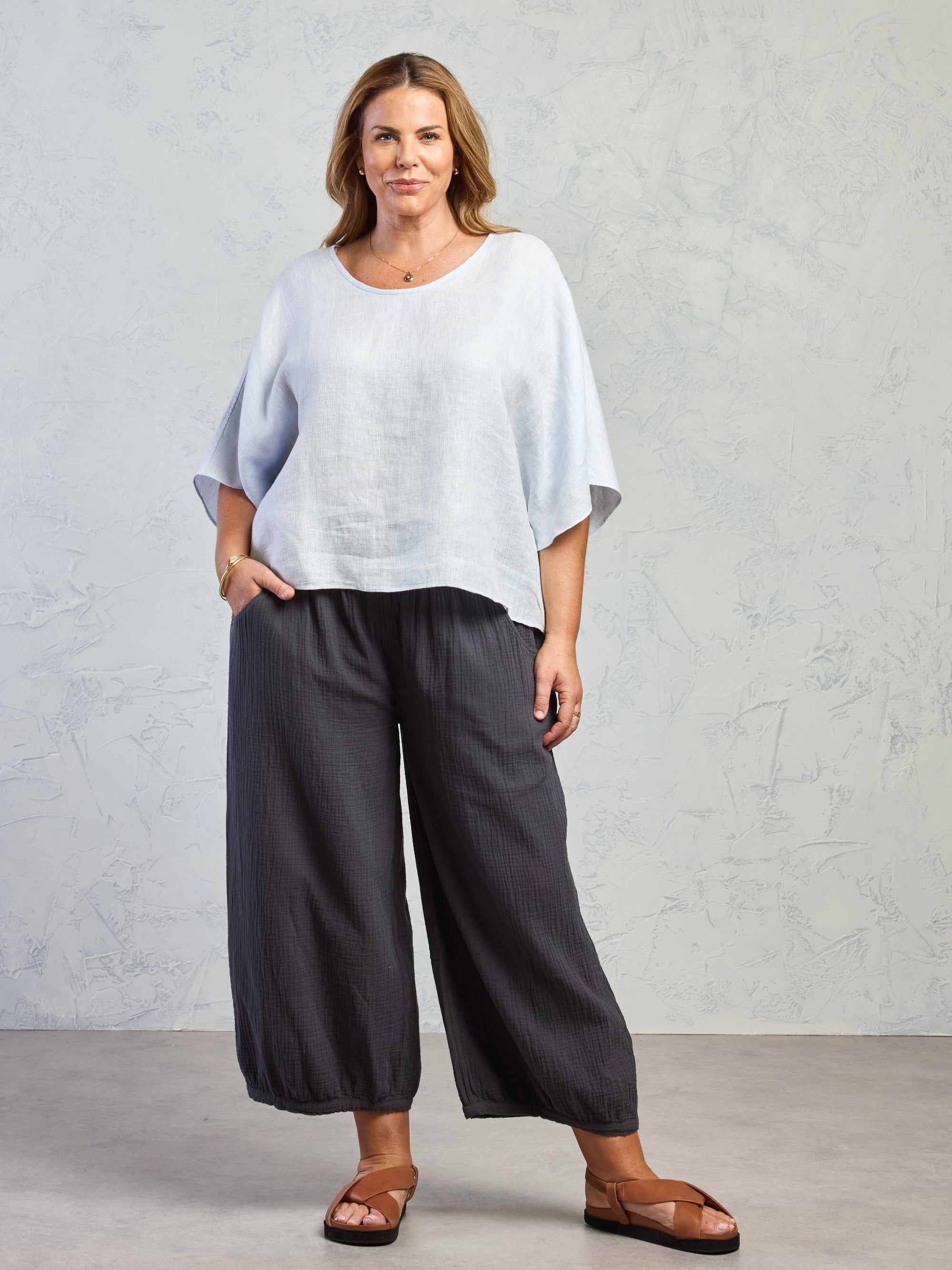 Woman wearing a light blue top and dark gray wide-leg pants against a plain background