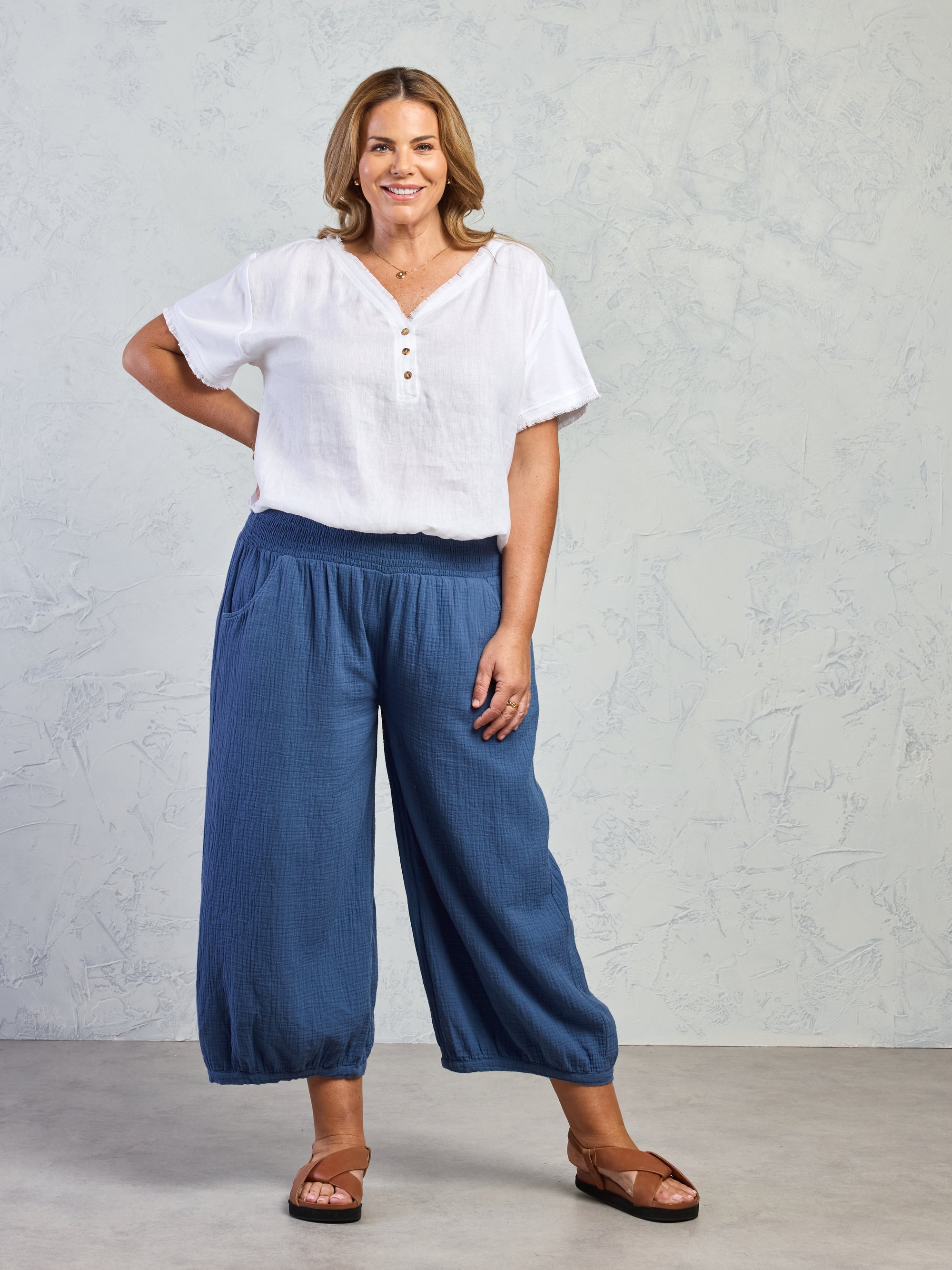 Woman wearing a white blouse and blue pants against a plain background