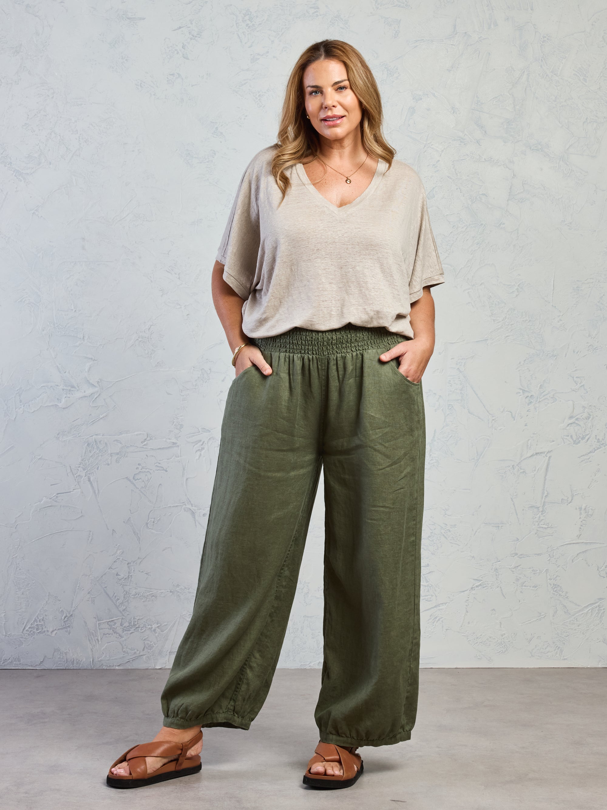 Woman wearing a beige top and green wide-leg pants against a gray background