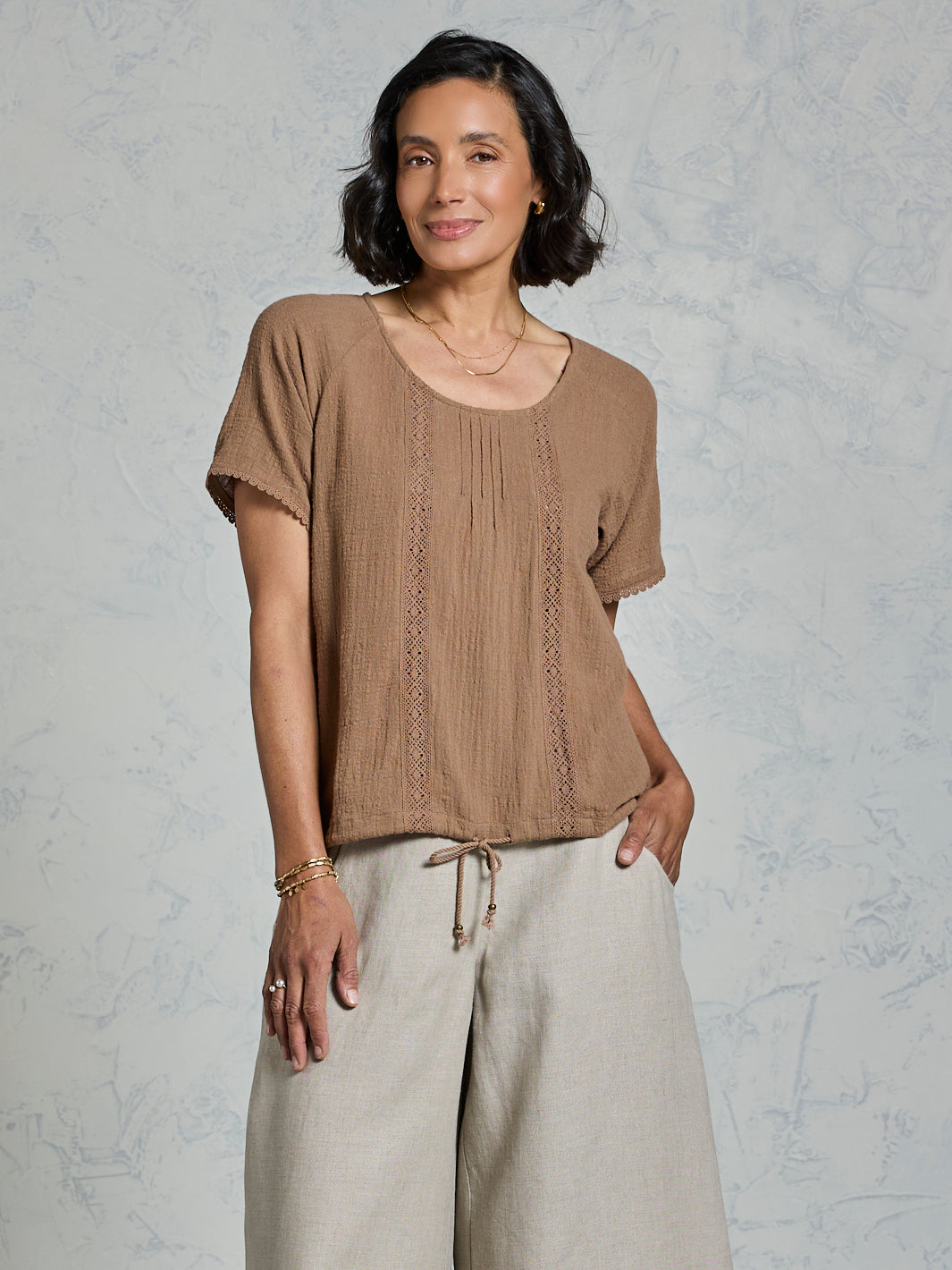 Woman wearing a brown top and beige pants against a gray background
