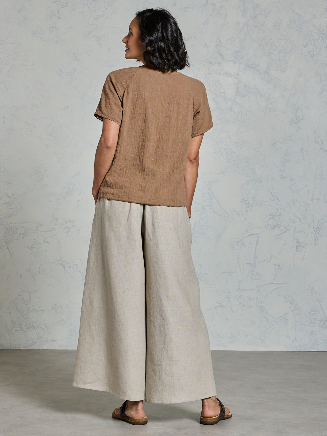 Person wearing a brown shirt and beige pants against a plain background