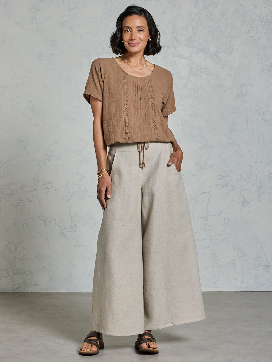 Woman wearing a brown top and beige wide-leg pants against a gray background