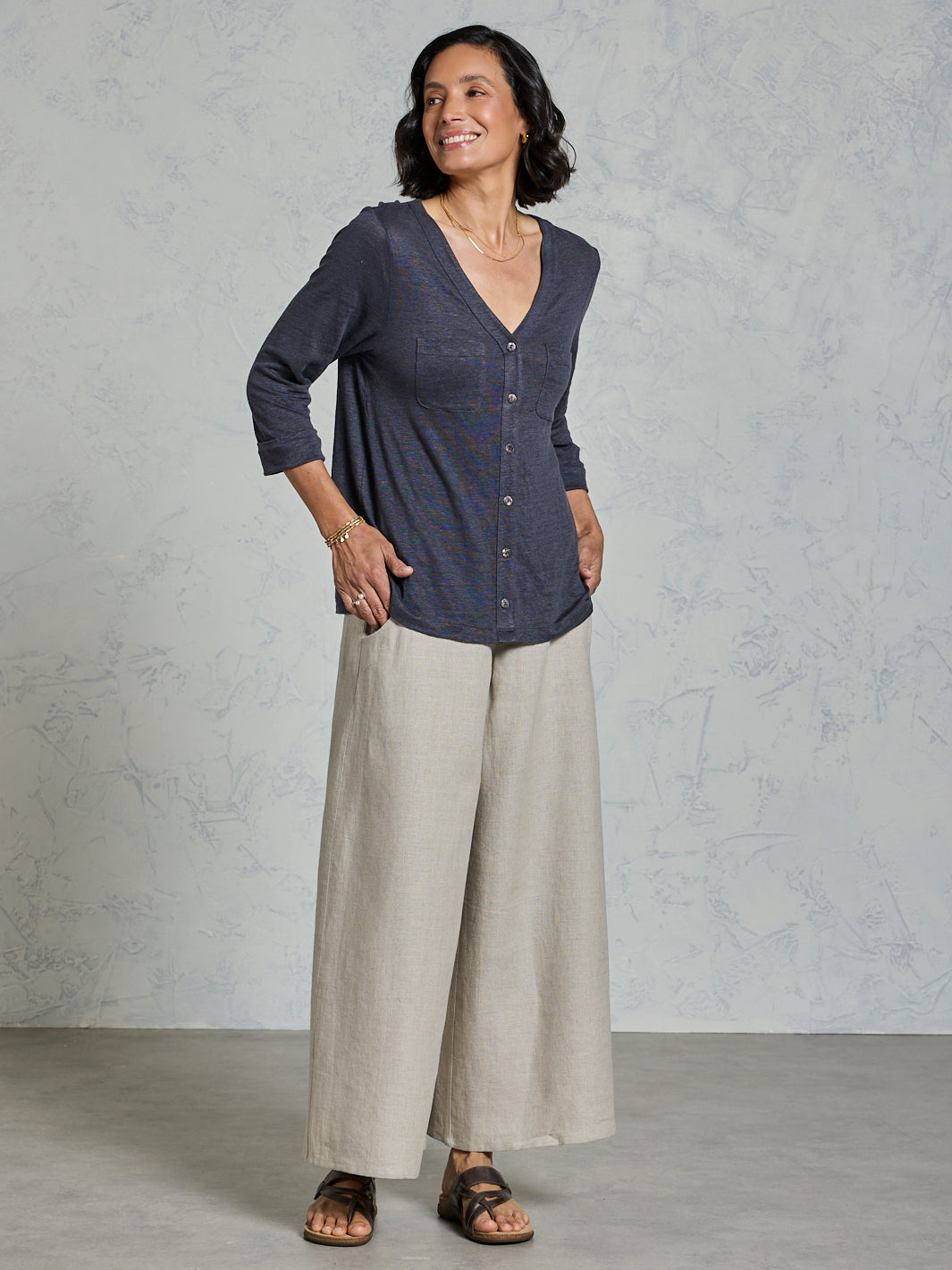 Woman wearing a dark blue shirt and beige pants against a gray background