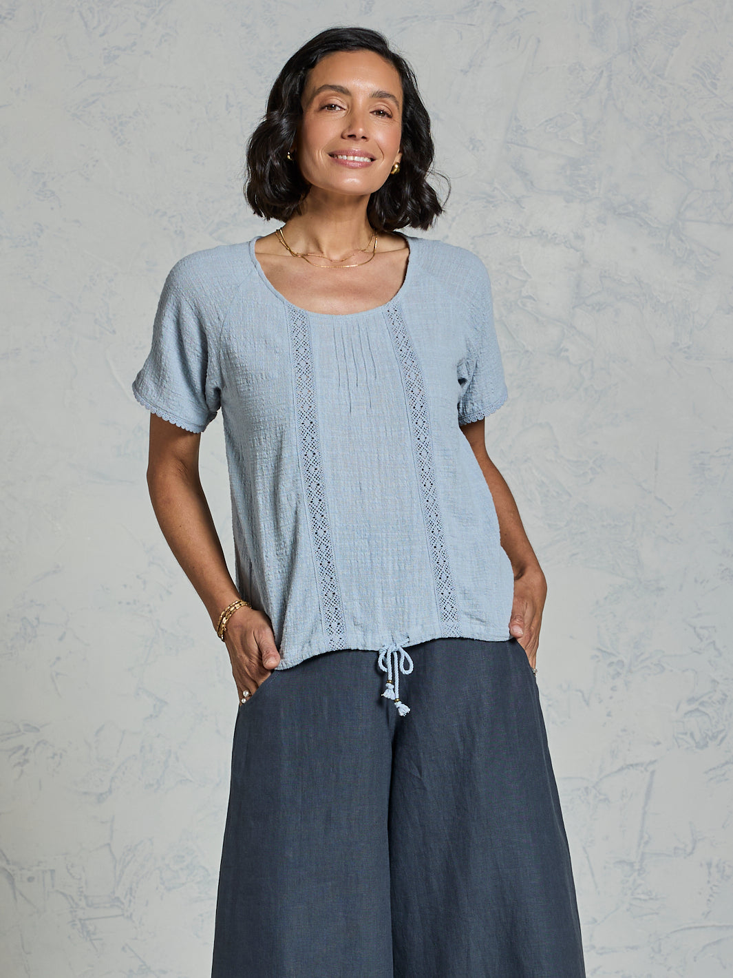 Woman wearing a light blue top and charcoal pants against a plain background