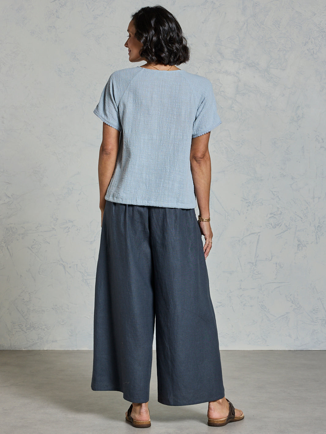 Person wearing a light blue top and charcoal wide-leg pants against a plain background