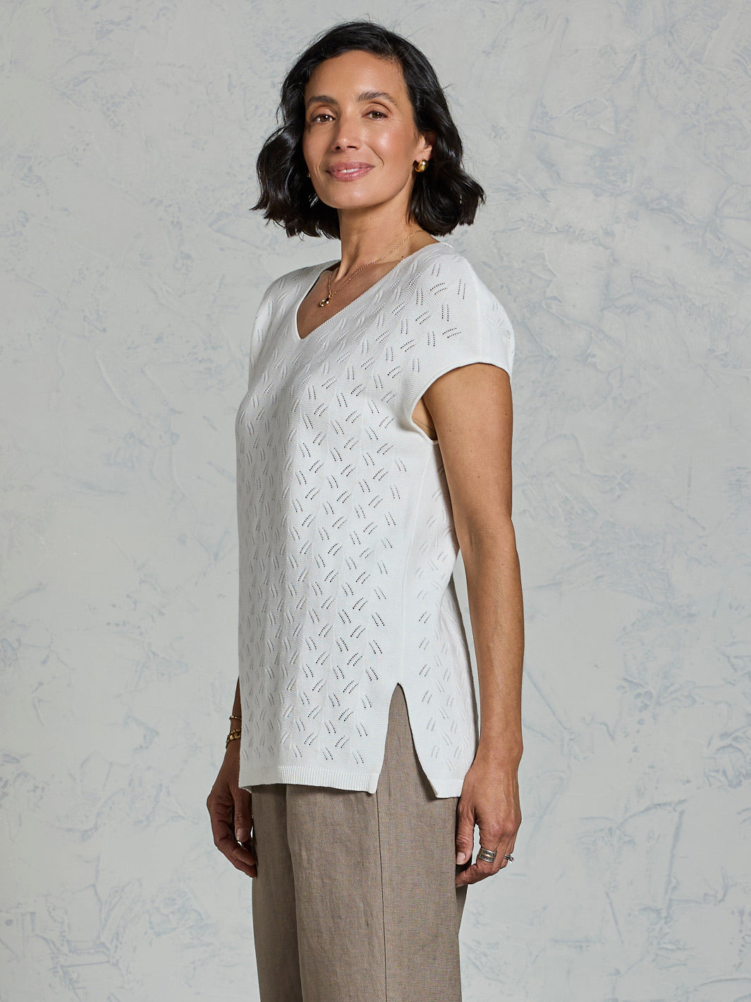 Woman wearing a white short-sleeve top with a textured pattern against a light gray background
