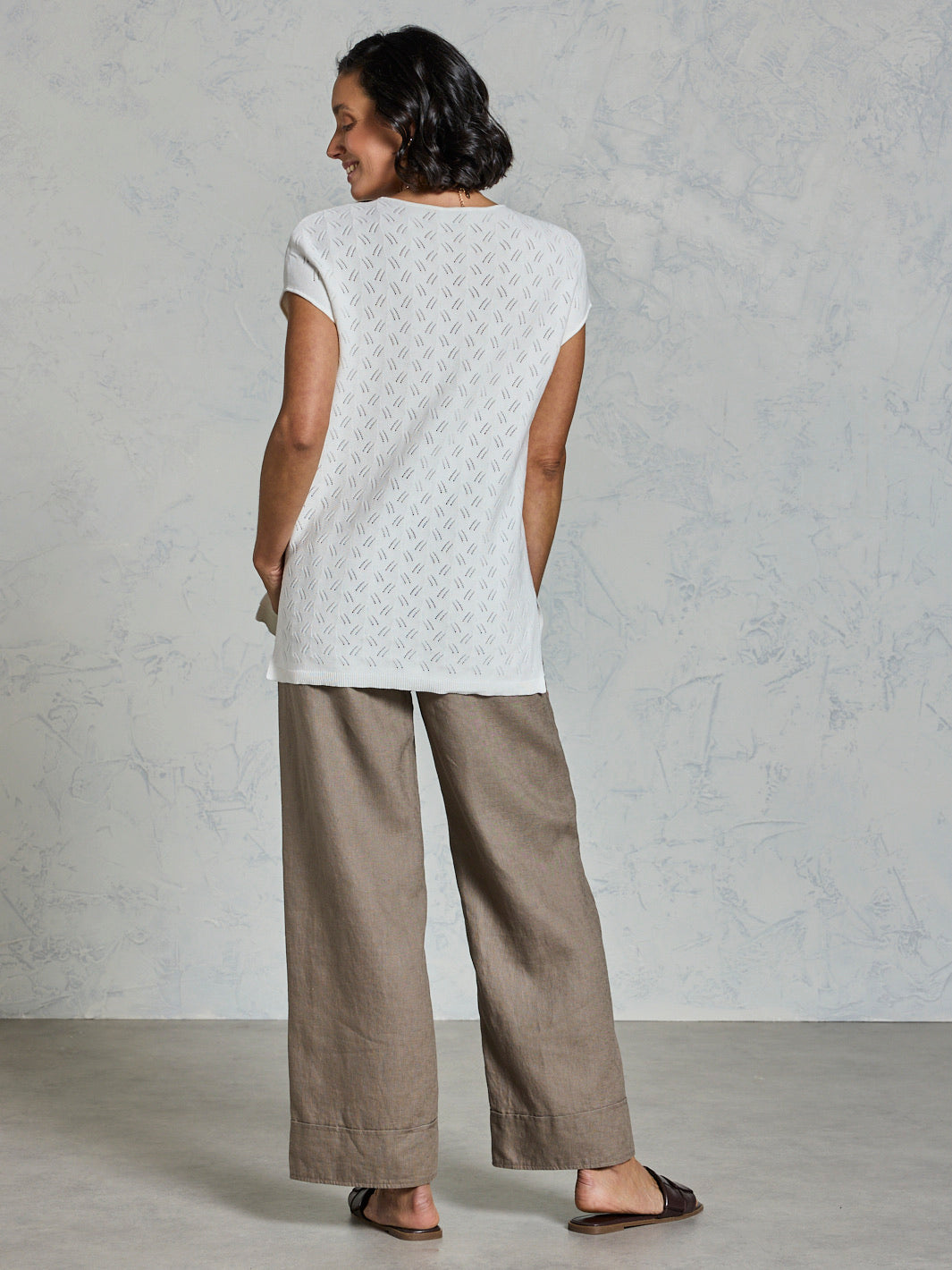 Woman wearing a white textured top and beige pants against a plain background