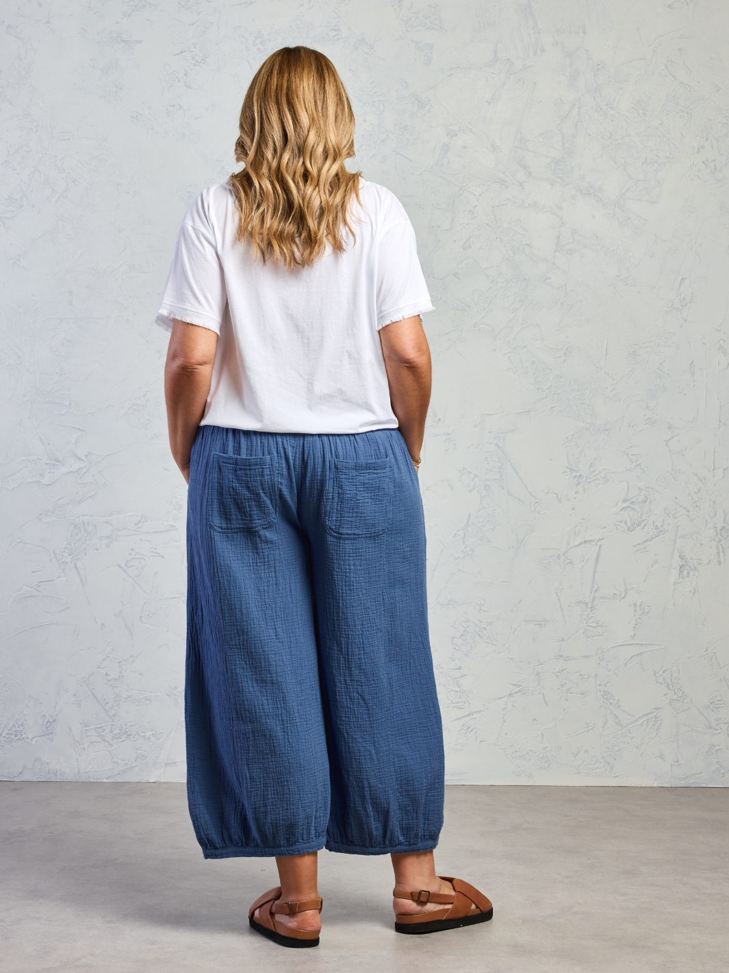 Person wearing a white t-shirt and blue wide-leg pants against a plain background