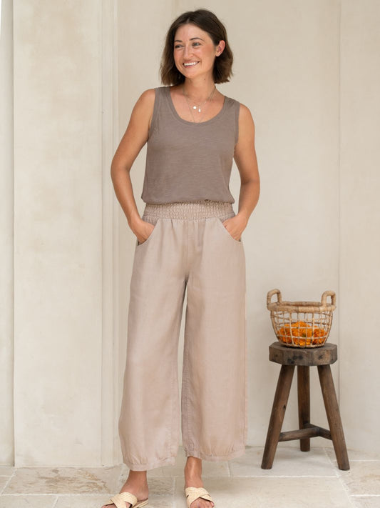 Woman wearing a sleeveless top and wide-leg pants standing next to a wooden stool with a basket.