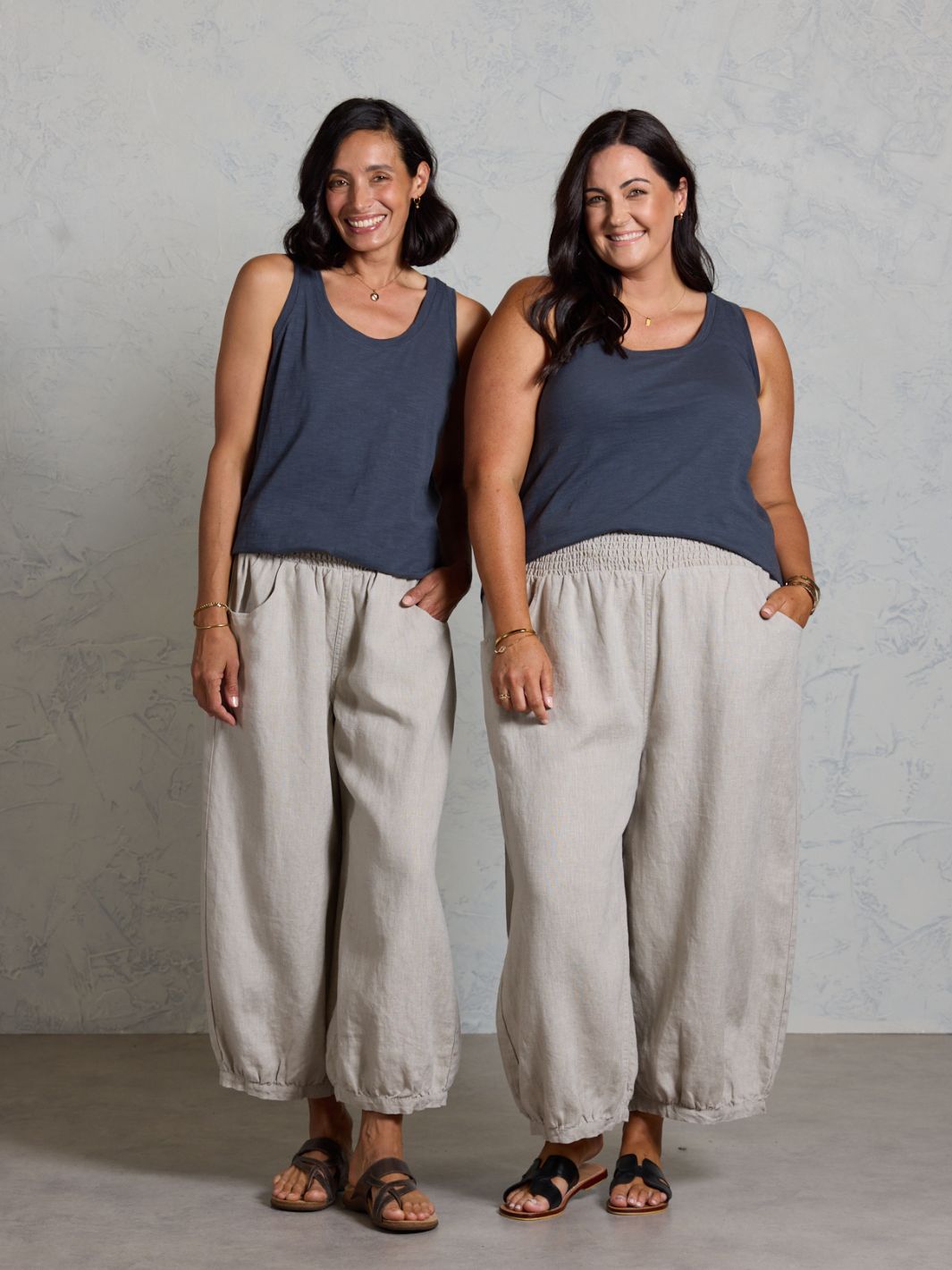 Two women wearing black tank tops and beige wide-leg pants standing against a plain background.