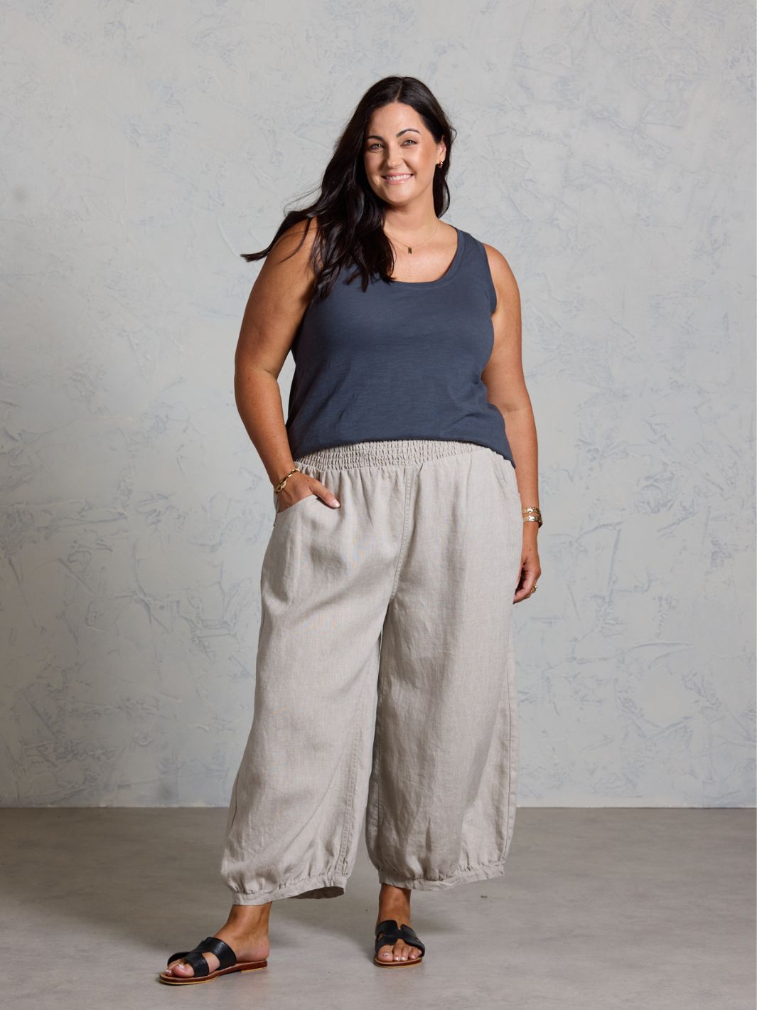 Woman wearing a black tank top and light gray wide-leg pants against a plain background