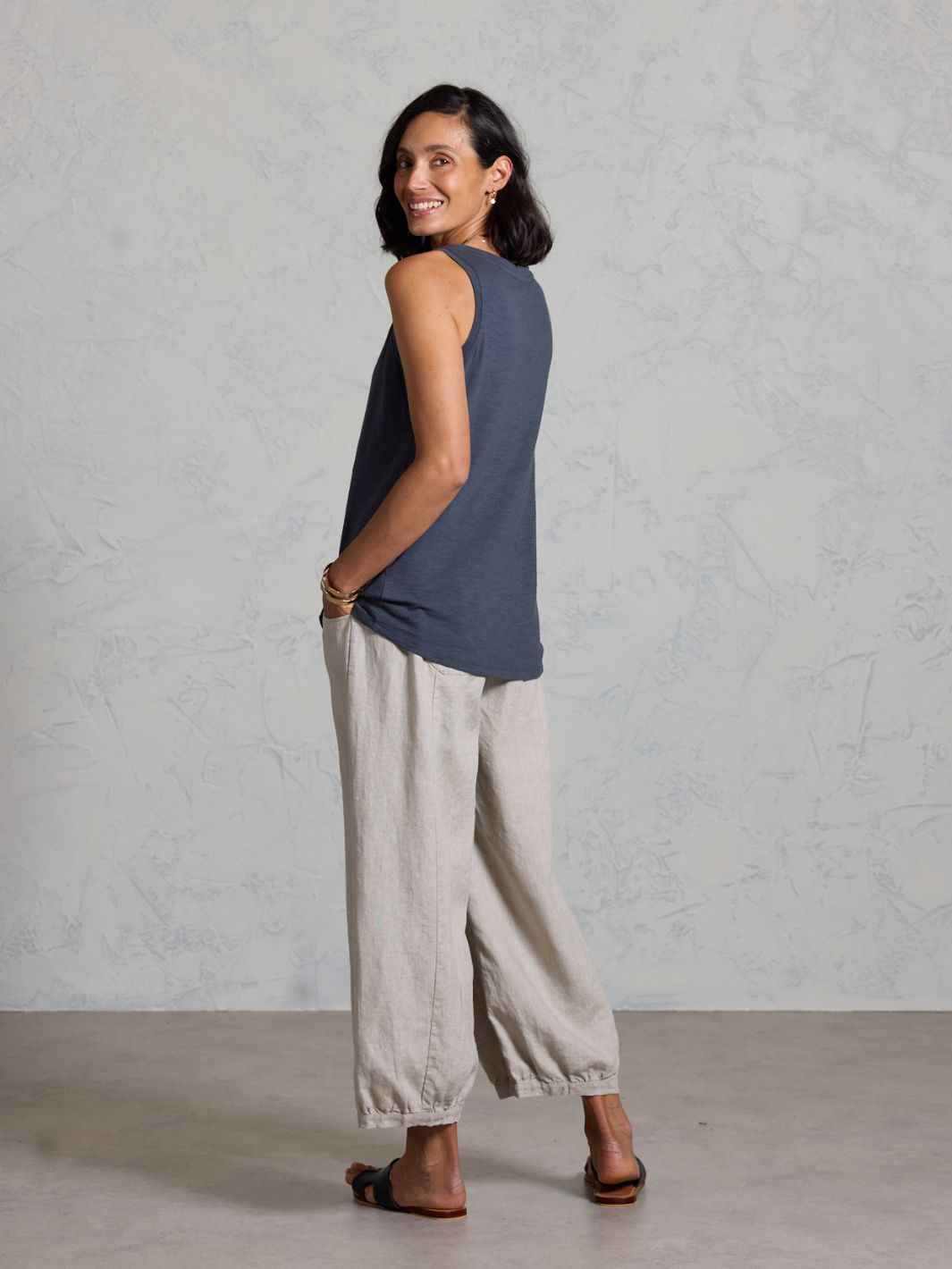 Woman wearing a black sleeveless top and beige pants against a plain background