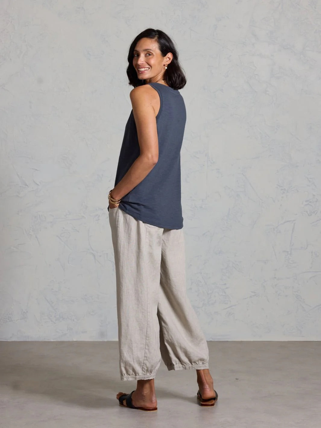 Woman wearing a sleeveless top and beige pants against a plain background
