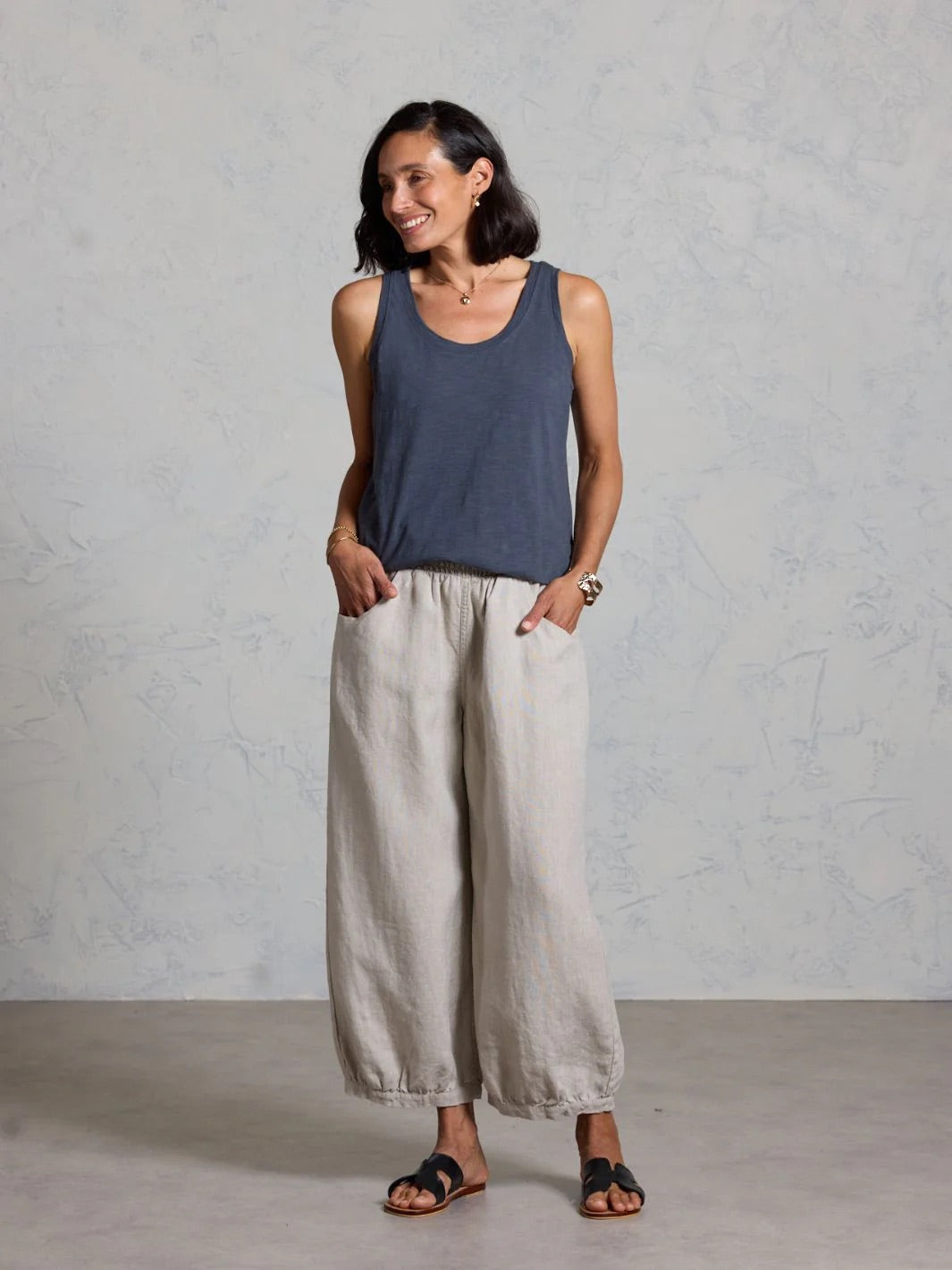 Woman wearing a dark tank top and beige wide-leg pants against a gray background