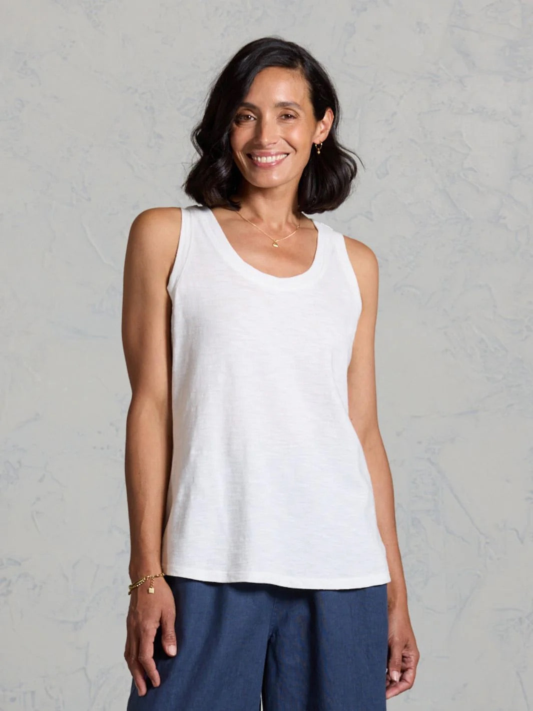 Woman wearing a white tank top and blue pants against a gray background