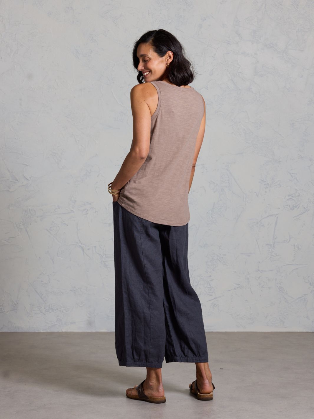 Woman wearing a sleeveless top and wide-leg pants against a plain background