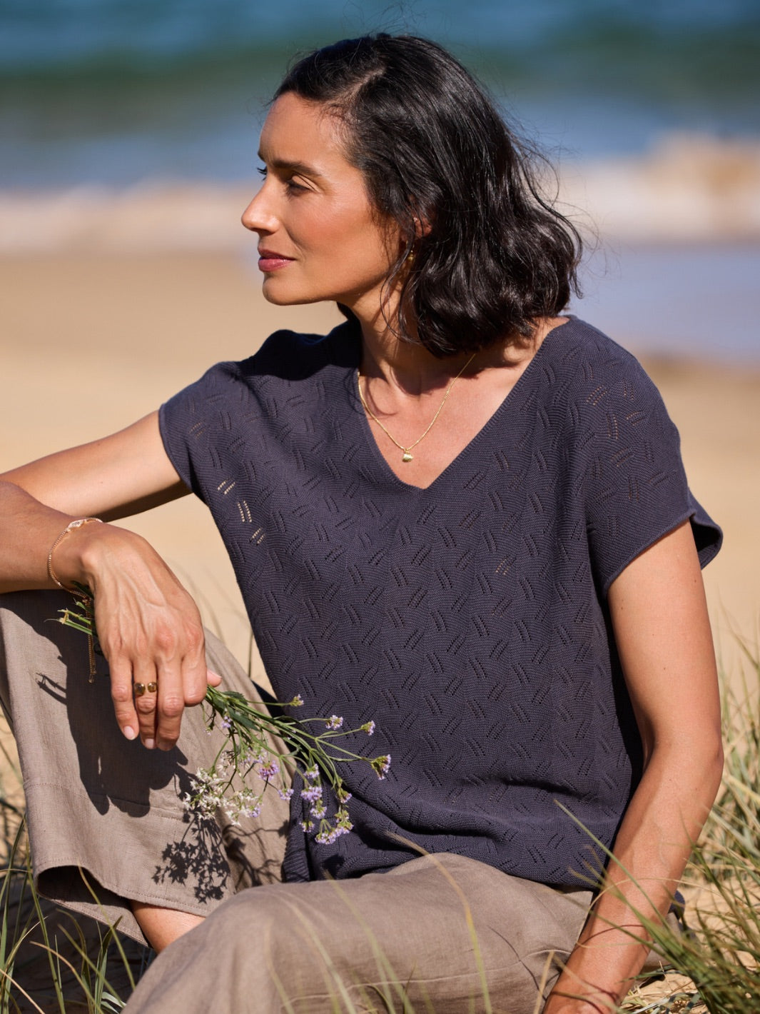 Woman sitting on a beach wearing a dark patterned shirt.