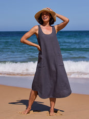 Woman in a drak dress and straw hat standing on a beach with ocean waves in the background