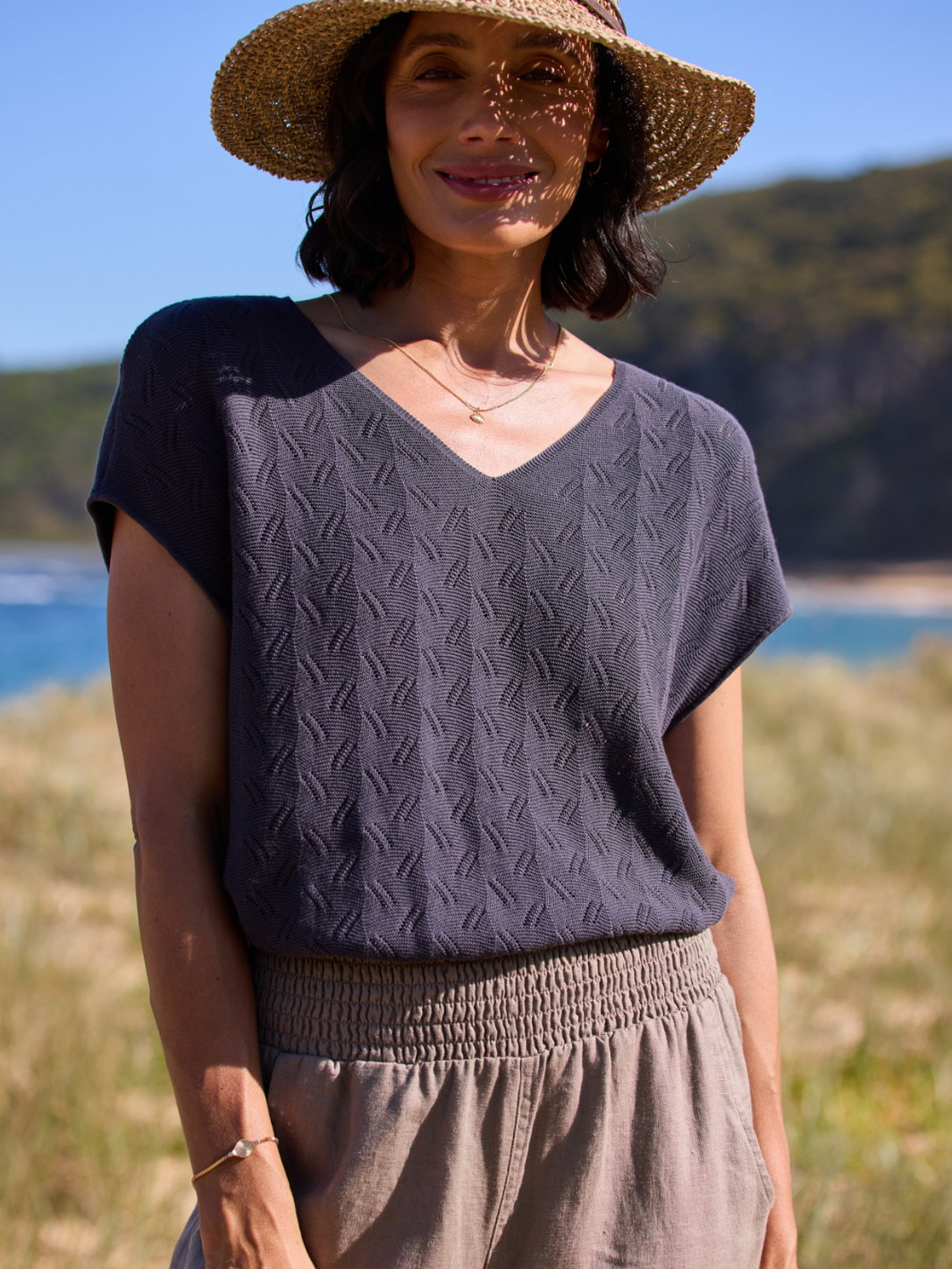 Woman wearing a dark knitted top and straw hat outdoors with a scenic background