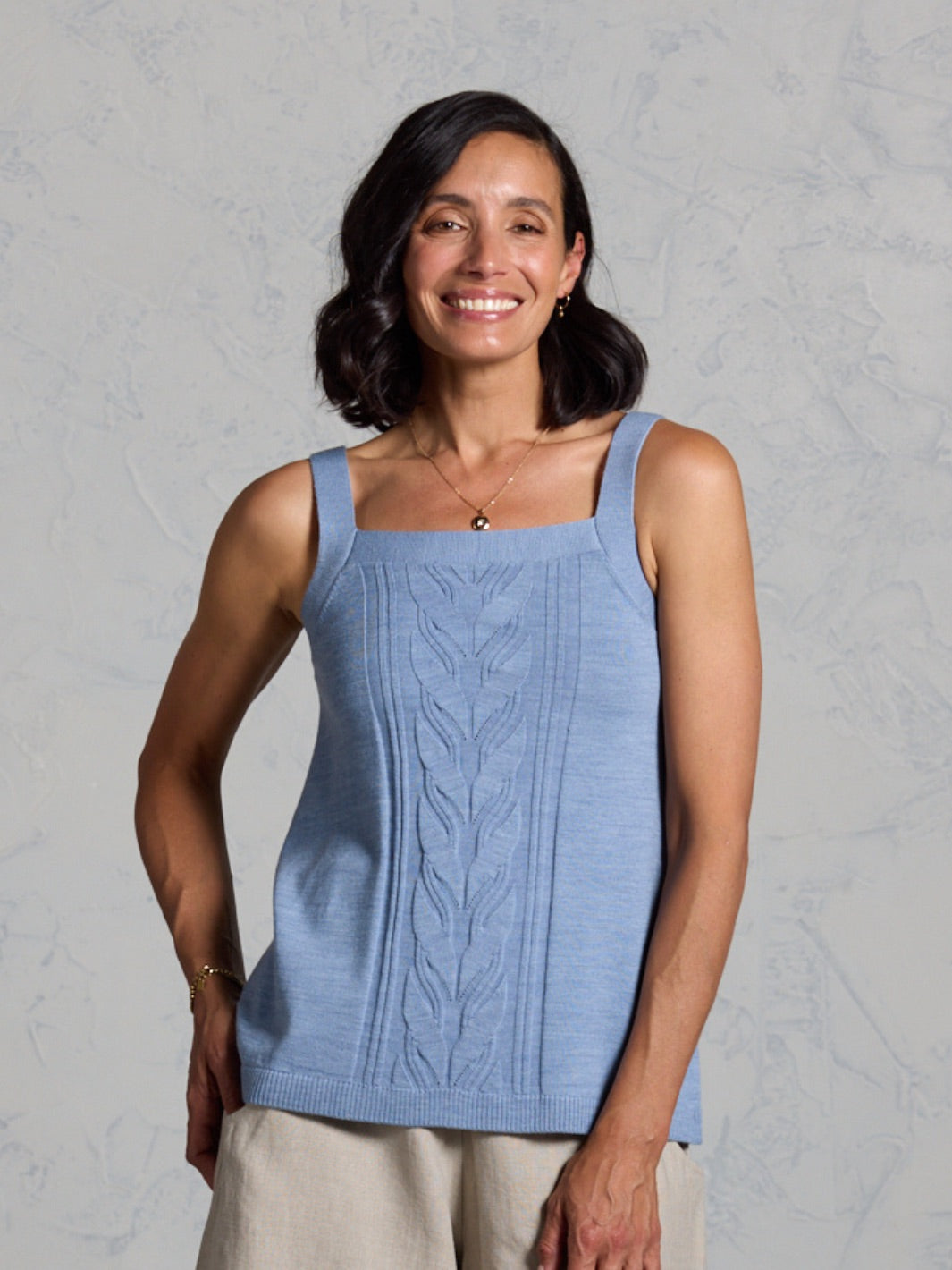Woman wearing a blue knitted tank top against a gray background