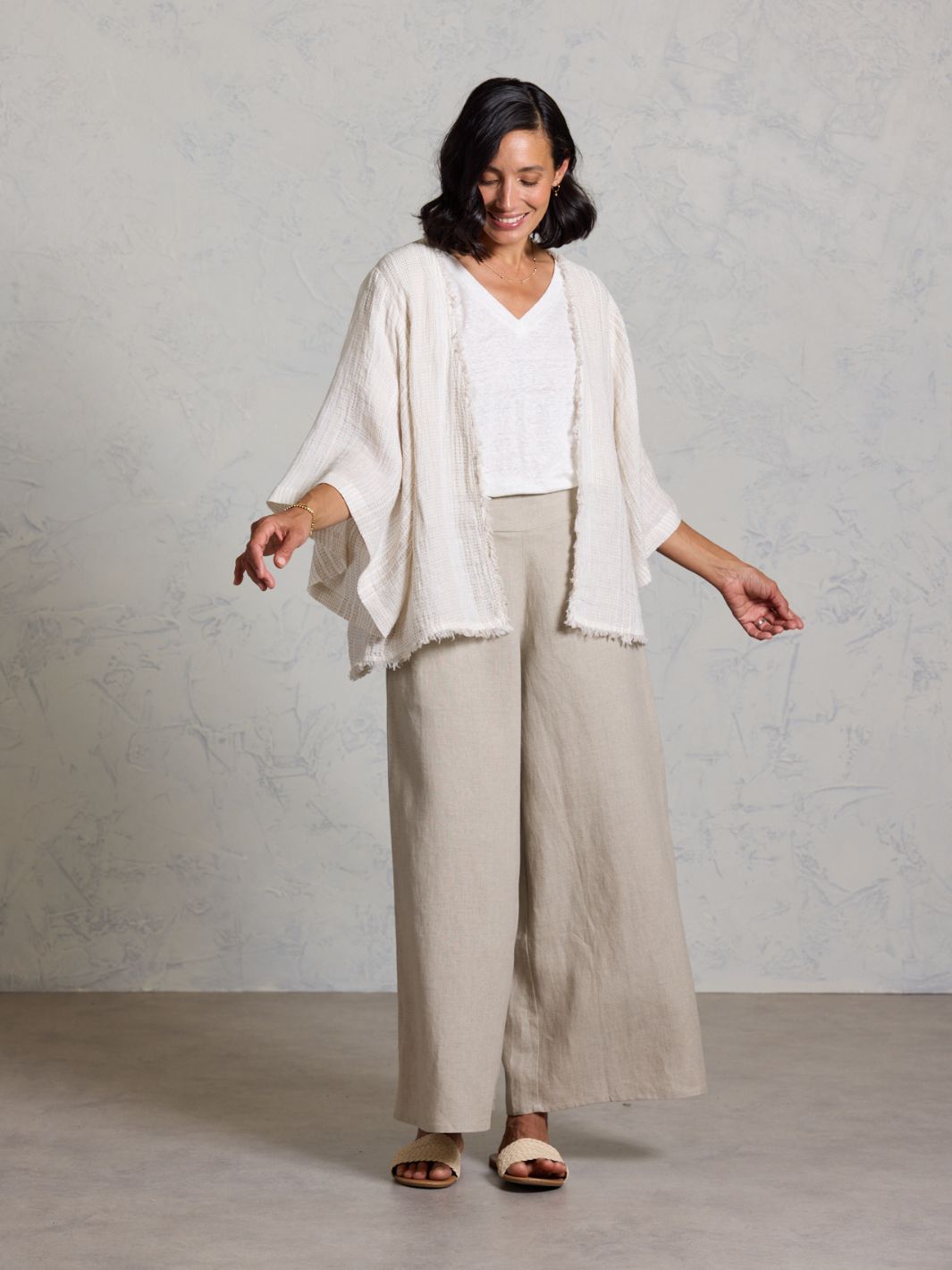 Woman wearing a white top and beige pants with a light beige cardigan against a gray background