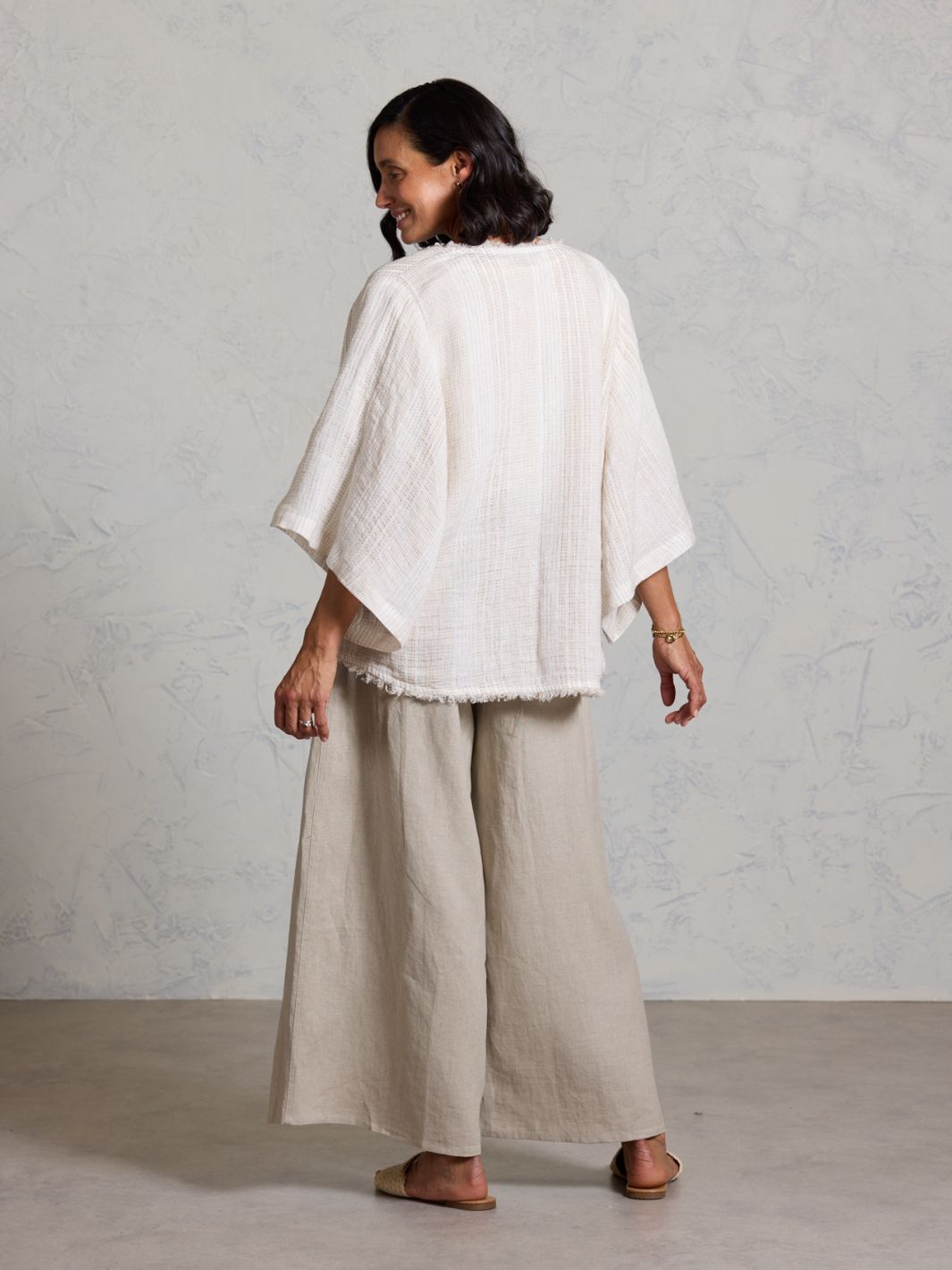 Woman wearing a white top and beige pants against a plain background