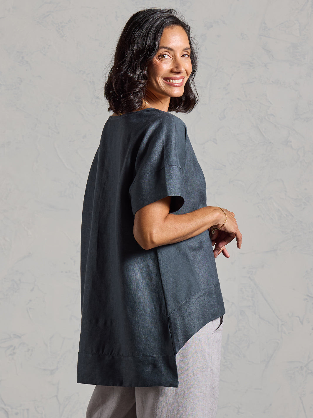 Woman wearing a dark tunic over light pants against a plain background