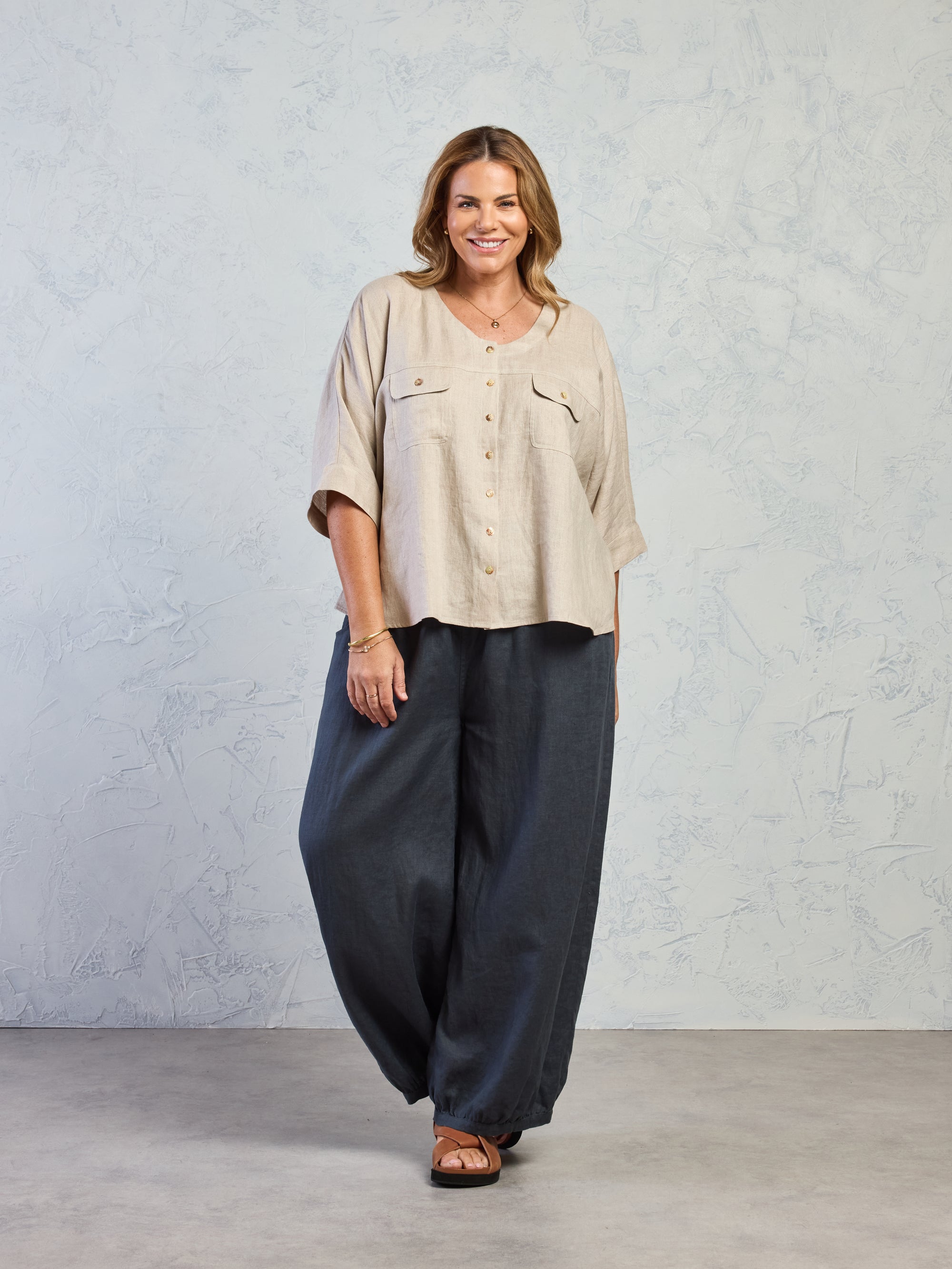 Woman wearing a beige shirt and dark pants against a gray background