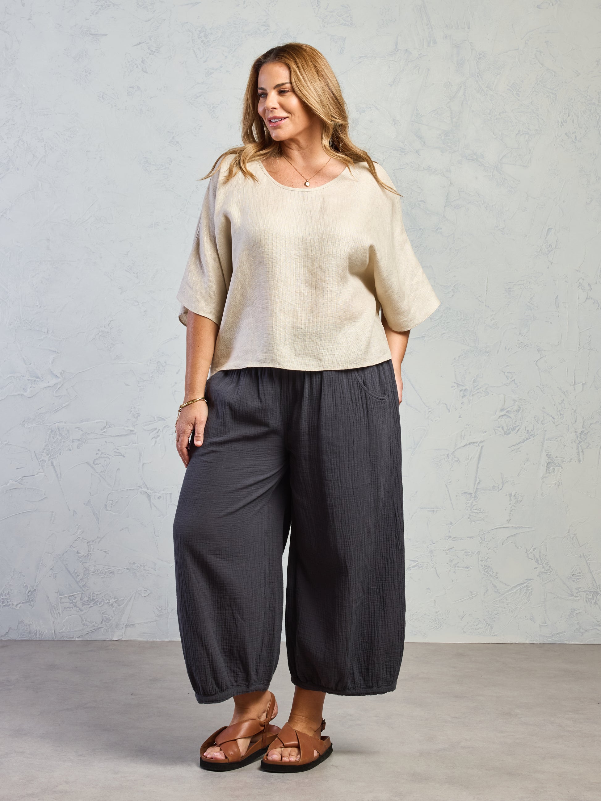 Woman wearing a beige top and dark pants against a gray background