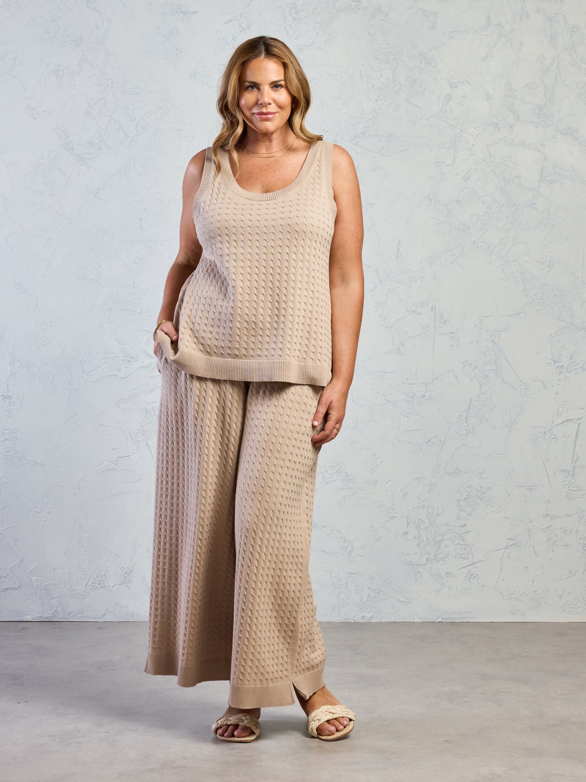 Woman wearing a beige sleeveless top and wide-leg pants against a plain background