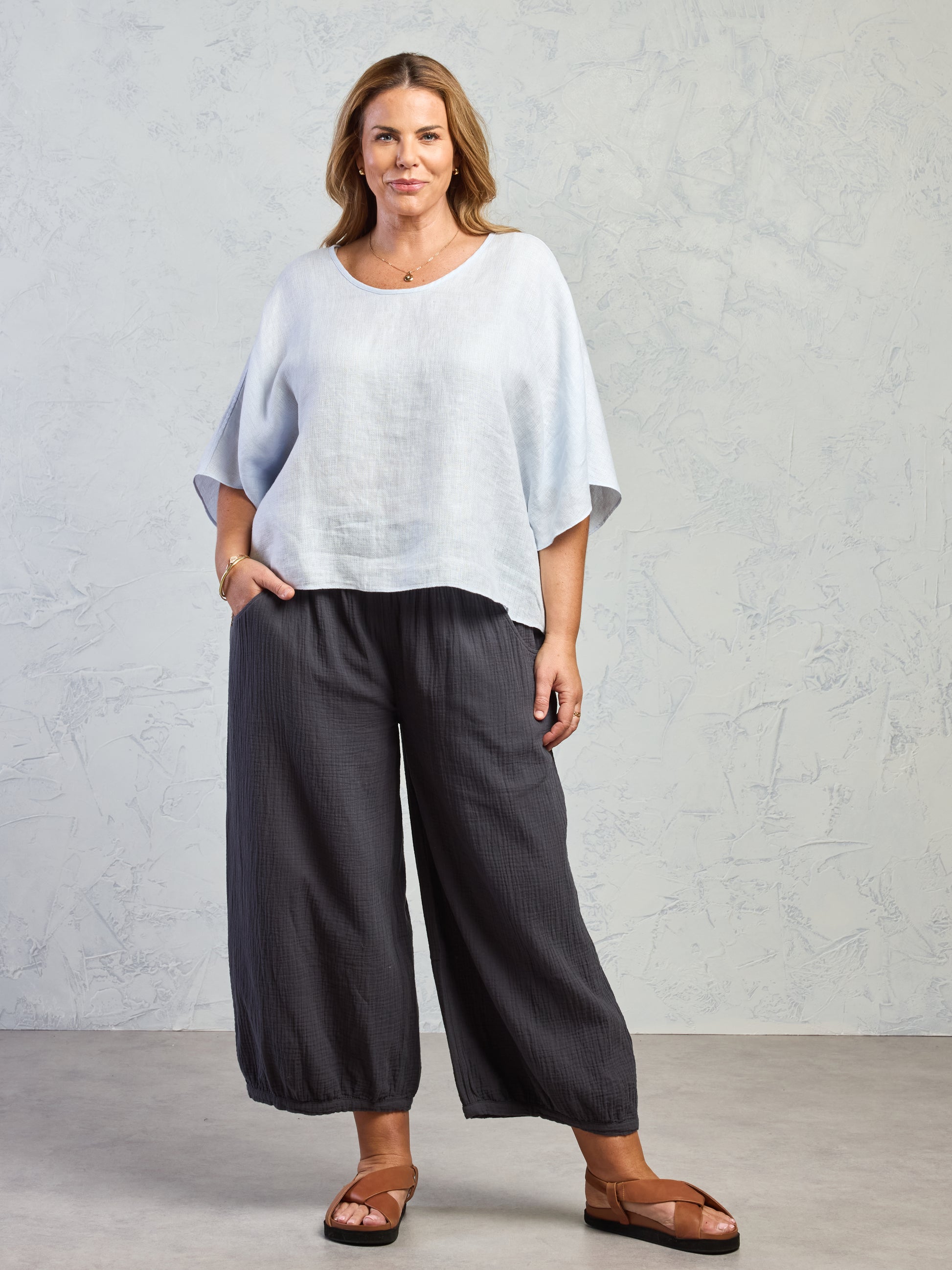 Woman wearing a light blue top and dark gray wide-leg pants against a plain background