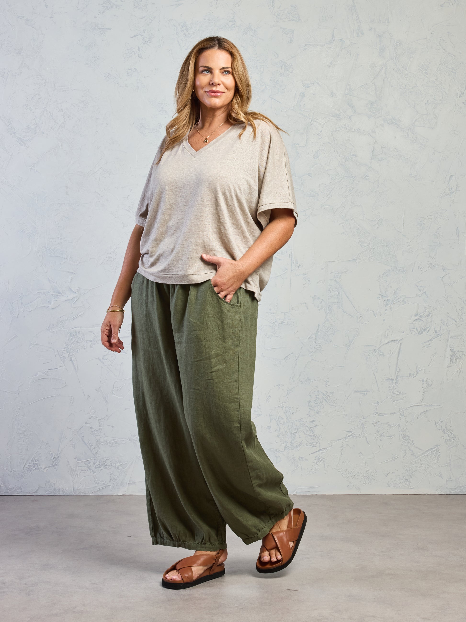 Woman wearing a beige top and green wide-leg pants against a plain background