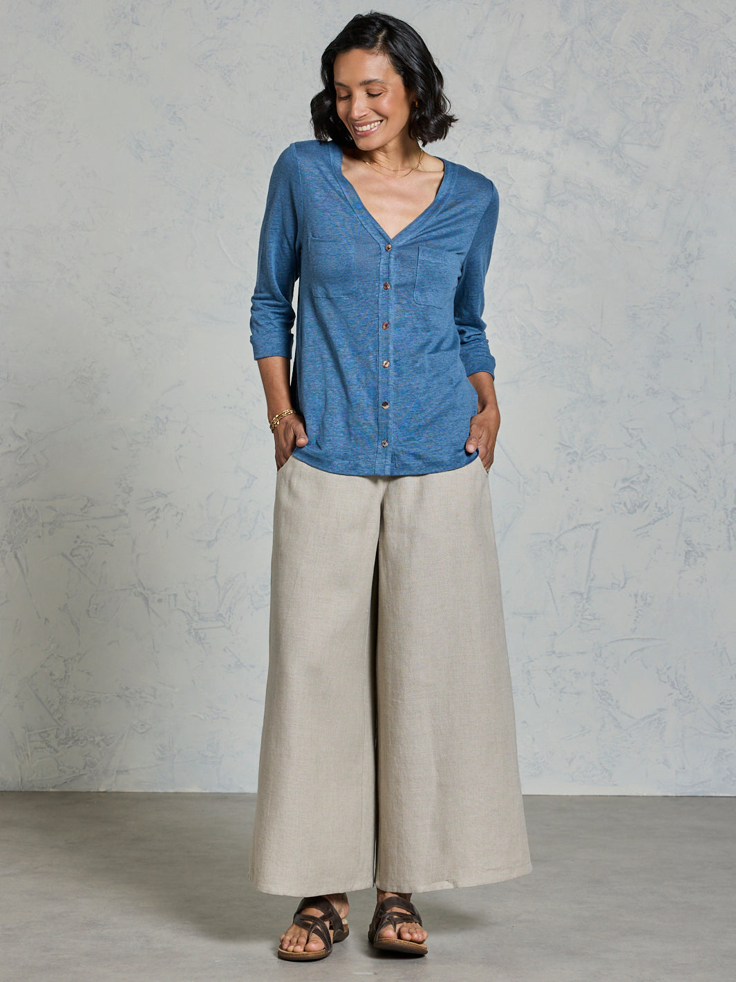Woman wearing a blue shirt and beige pants against a gray background