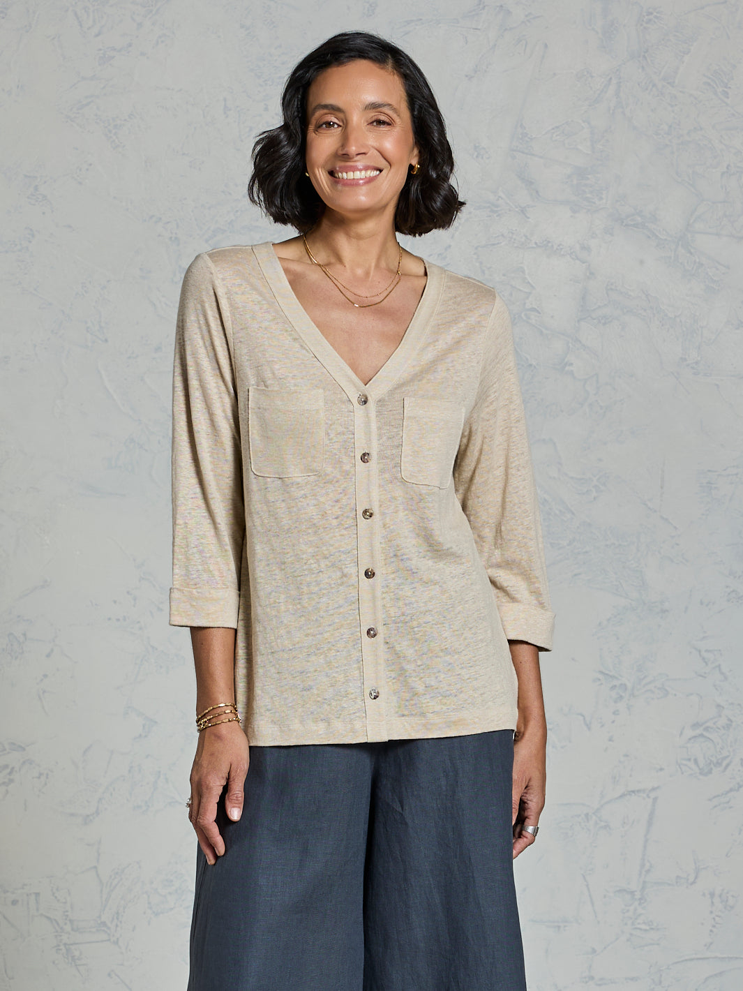 Woman wearing a beige button-up shirt and dark pants against a gray background