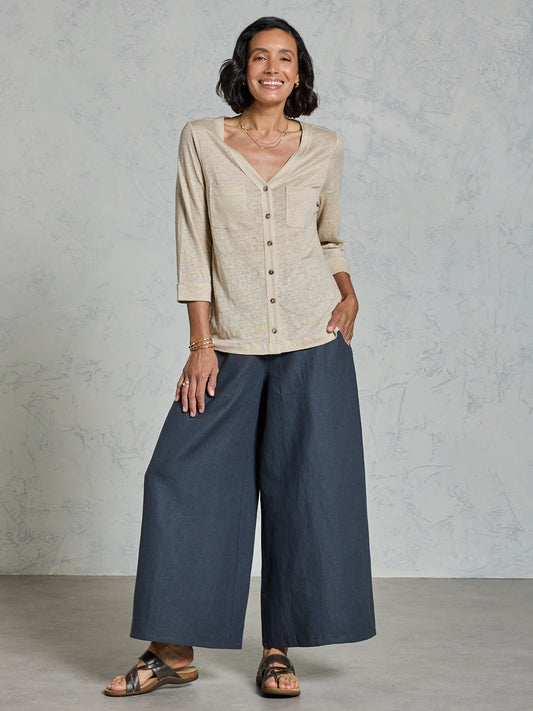 Woman wearing a beige shirt and blue pants against a gray background
