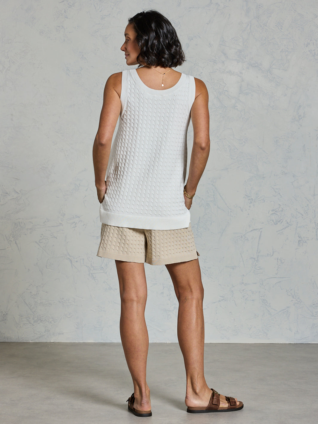 Person wearing a white sleeveless top and beige shorts against a gray background